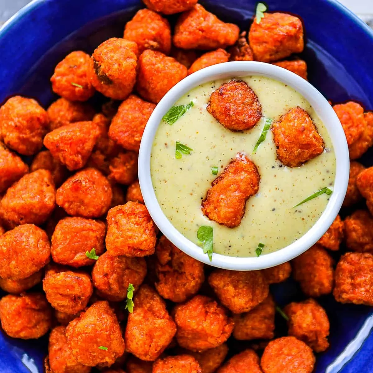 Fried buffalo chicken nuggets with a side of creamy ranch dipping sauce garnished with chopped green herbs.