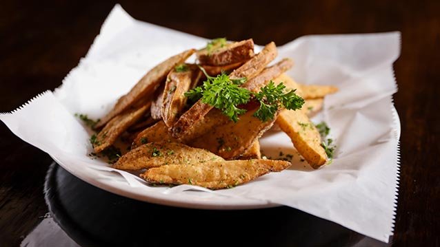 Fried potato wedges garnished with fresh parsley served on a white paper-lined black plate.