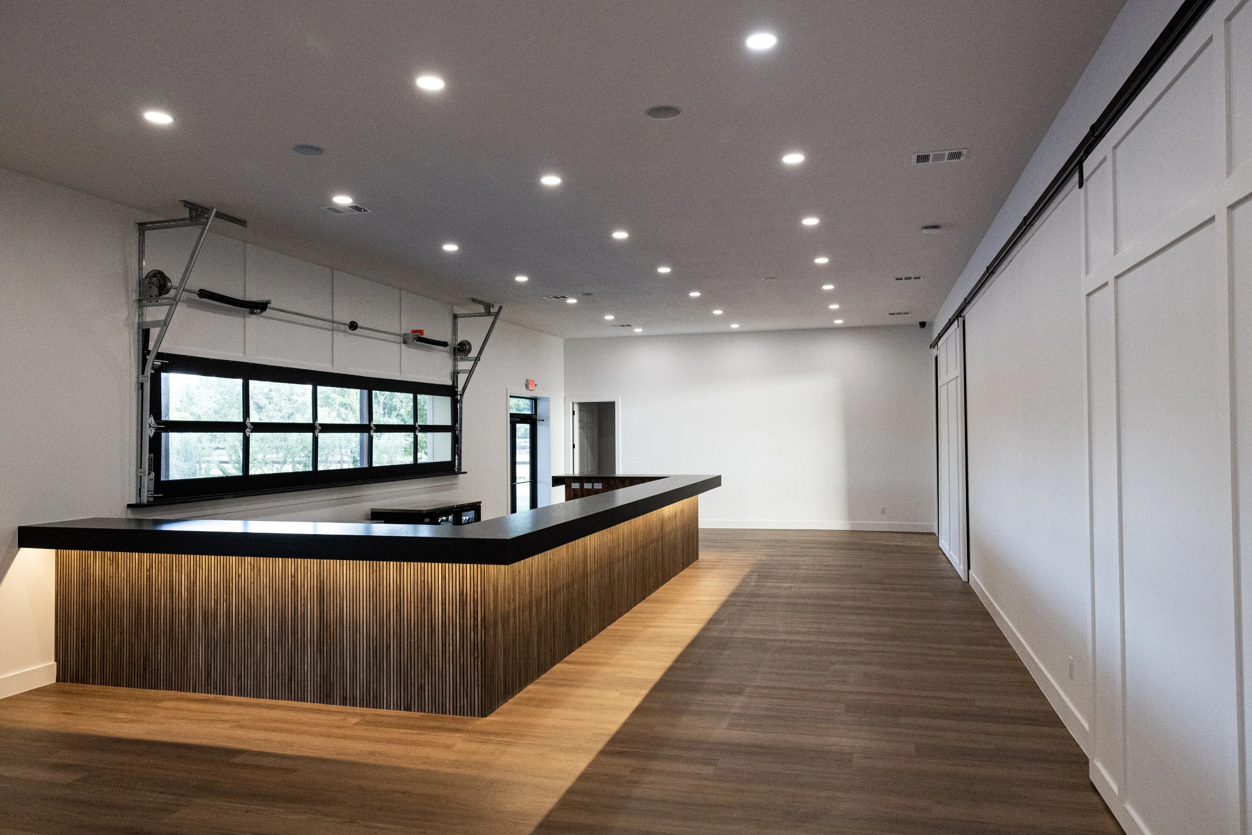 Interior of a modern, minimalistic room with a wooden reception desk, white walls, large window, and ceiling lights.