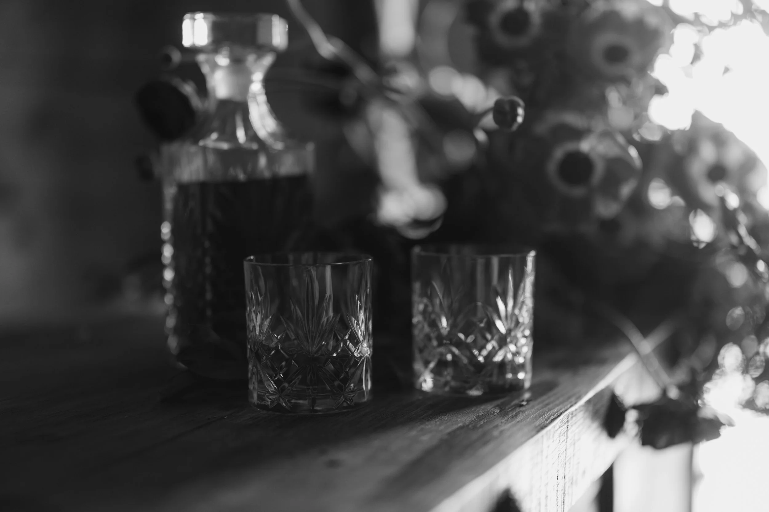 Three crystal glasses with intricate patterns on a wooden surface, with blurred decorative elements in the background.