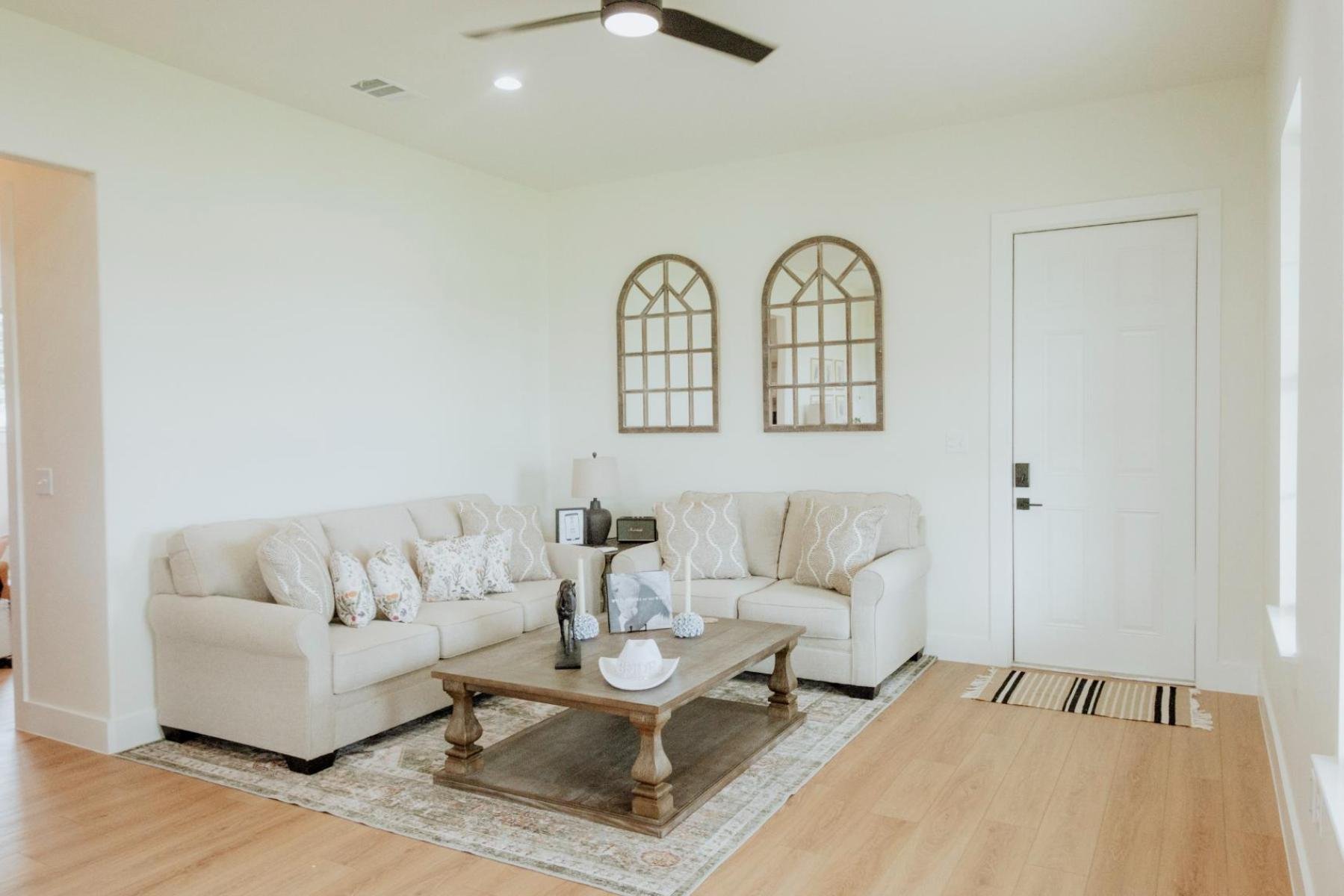 Living room with a beige sectional sofa, decorative pillows, a wooden coffee table with decorative items, and wall mirrors with arched frames.