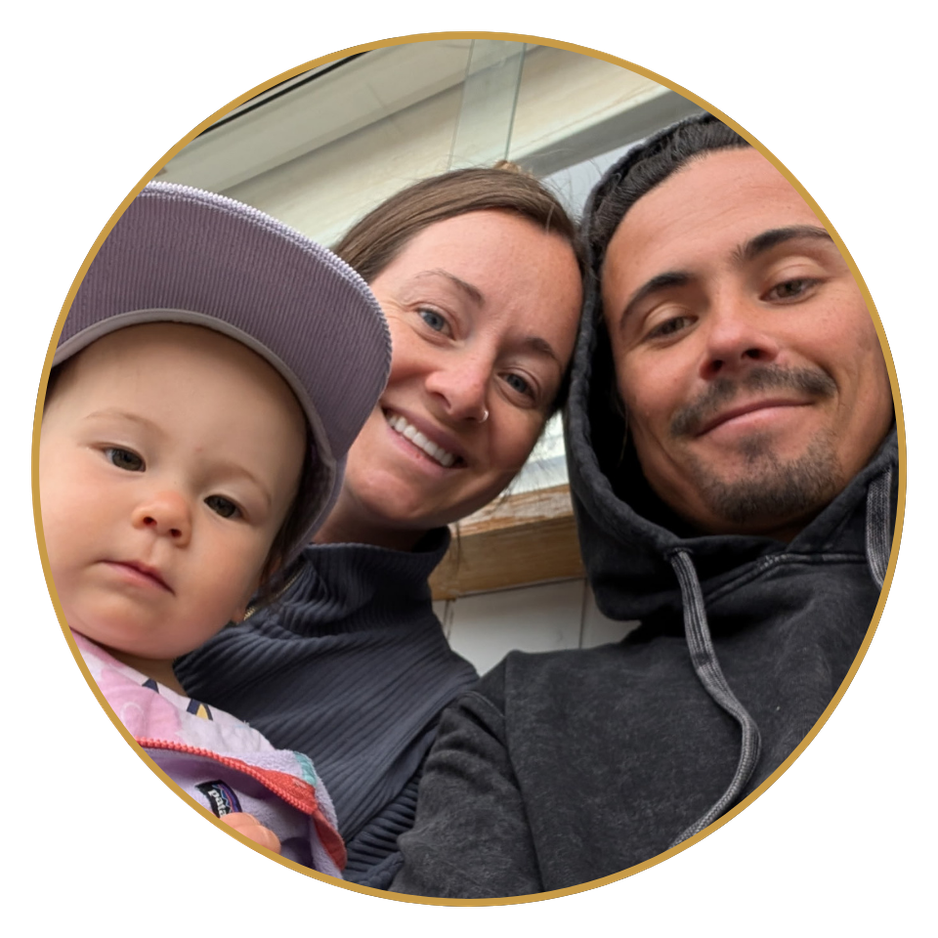 A family of three smiling closely together, including a young child wearing a cap, a woman with a nose ring, and a man in a hoodie, taking a selfie indoors.