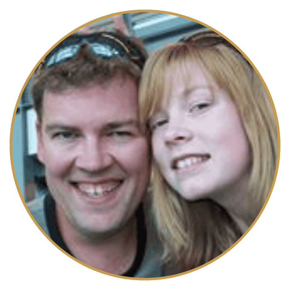 Close-up of a smiling man with sunglasses on his head and a woman with red hair making a playful face.