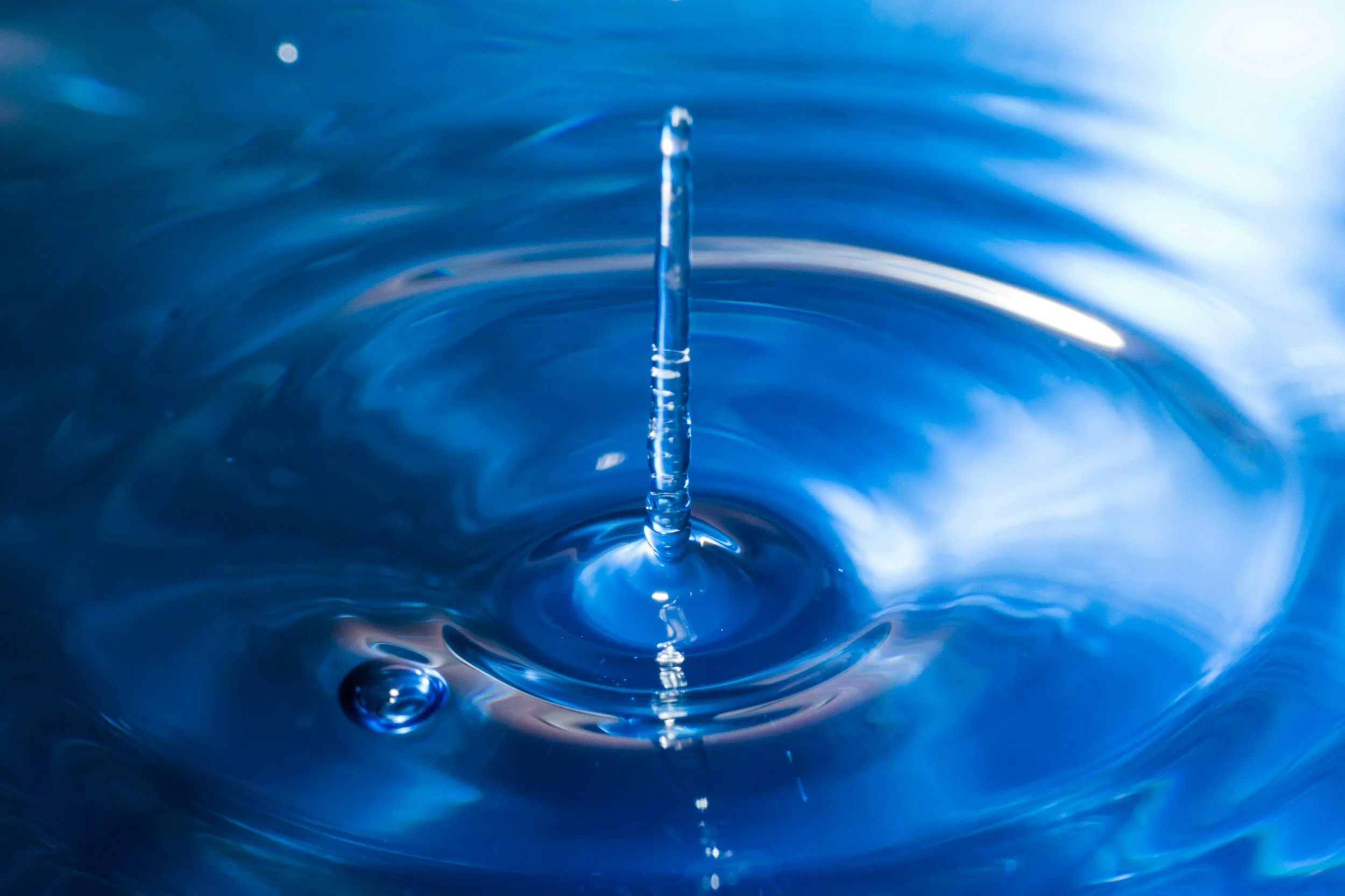 Close-up of a water droplet falling into a body of water, creating ripples and splashes with a blue background.