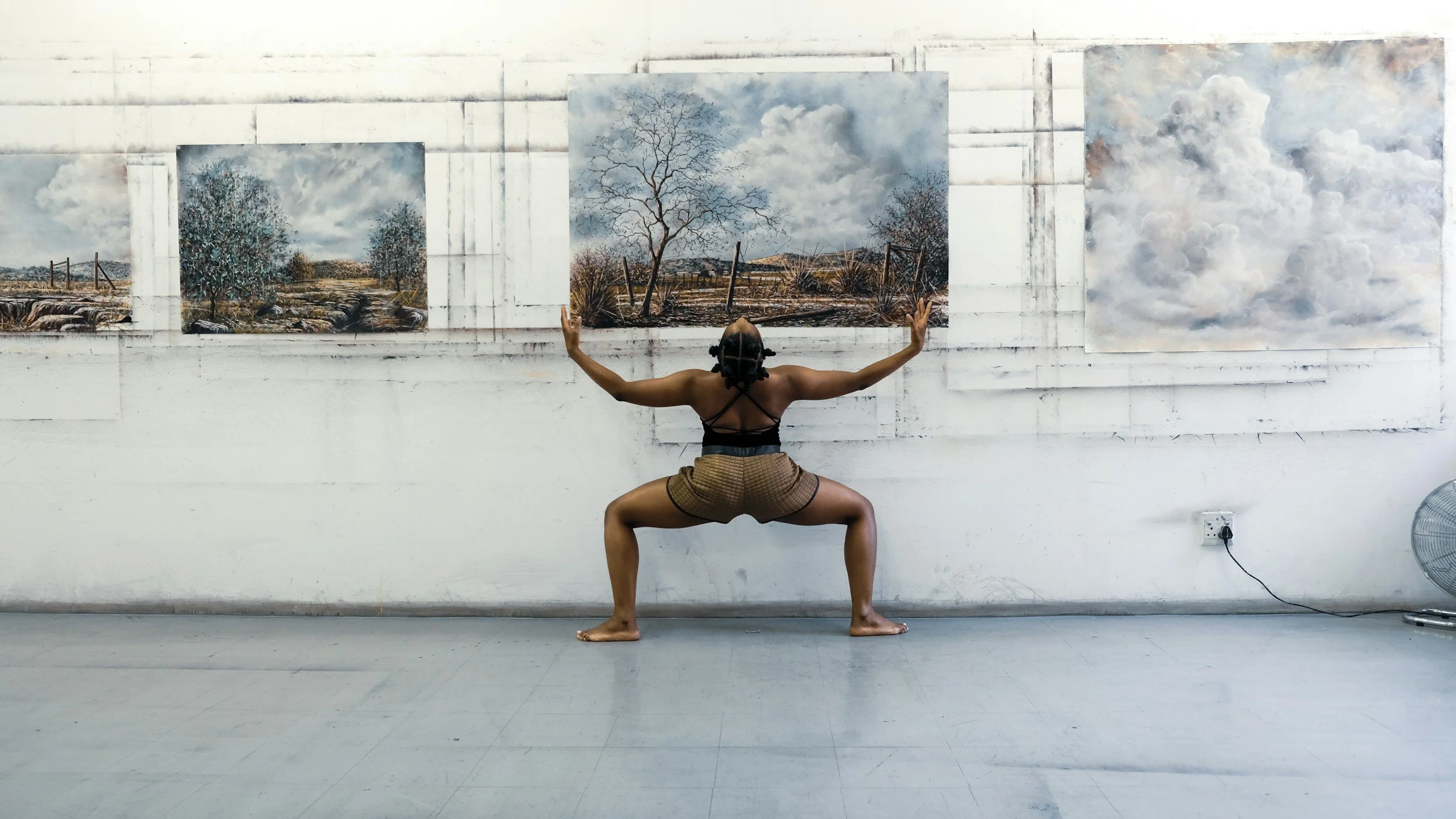 A person practicing yoga in front of landscape paintings in an art gallery.