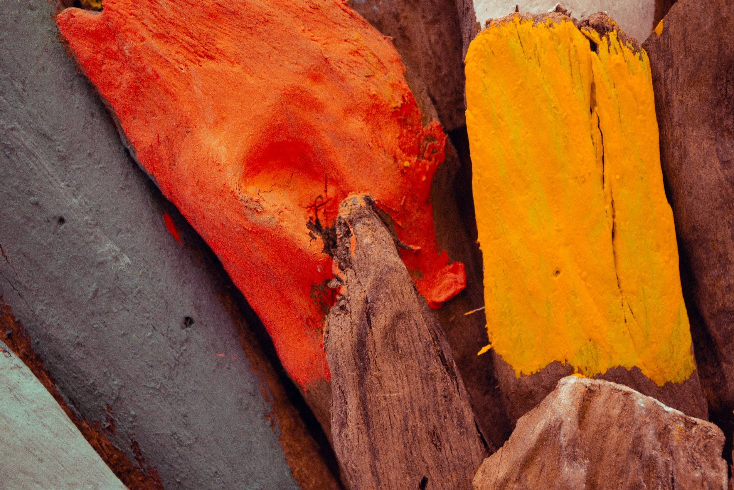Close-up of weathered orange, yellow, and brown painted wood pieces stacked together.