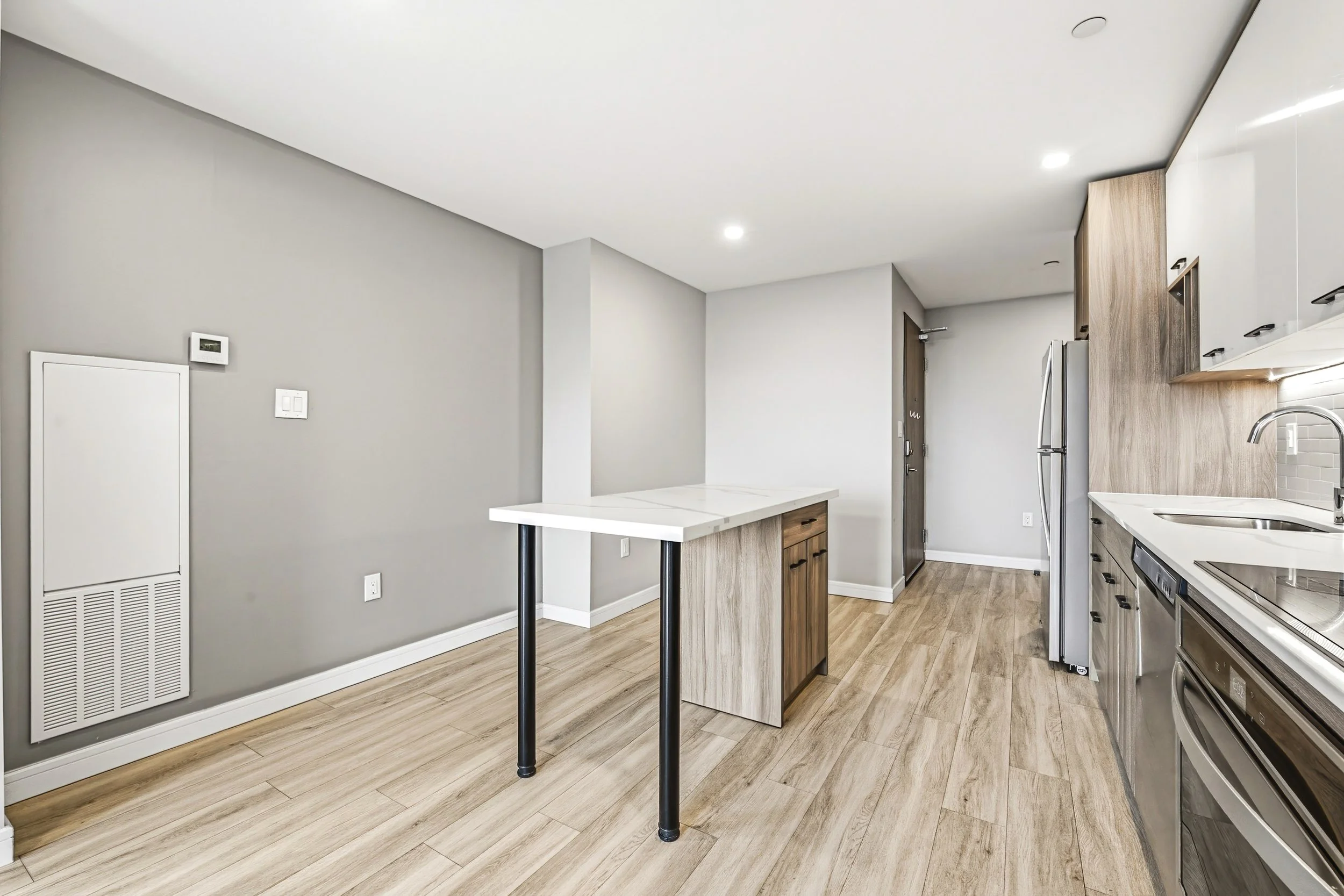 Modern kitchen with light wood flooring, gray walls, white ceiling, and built-in appliances. Includes a small island with a white countertop and black metal legs.