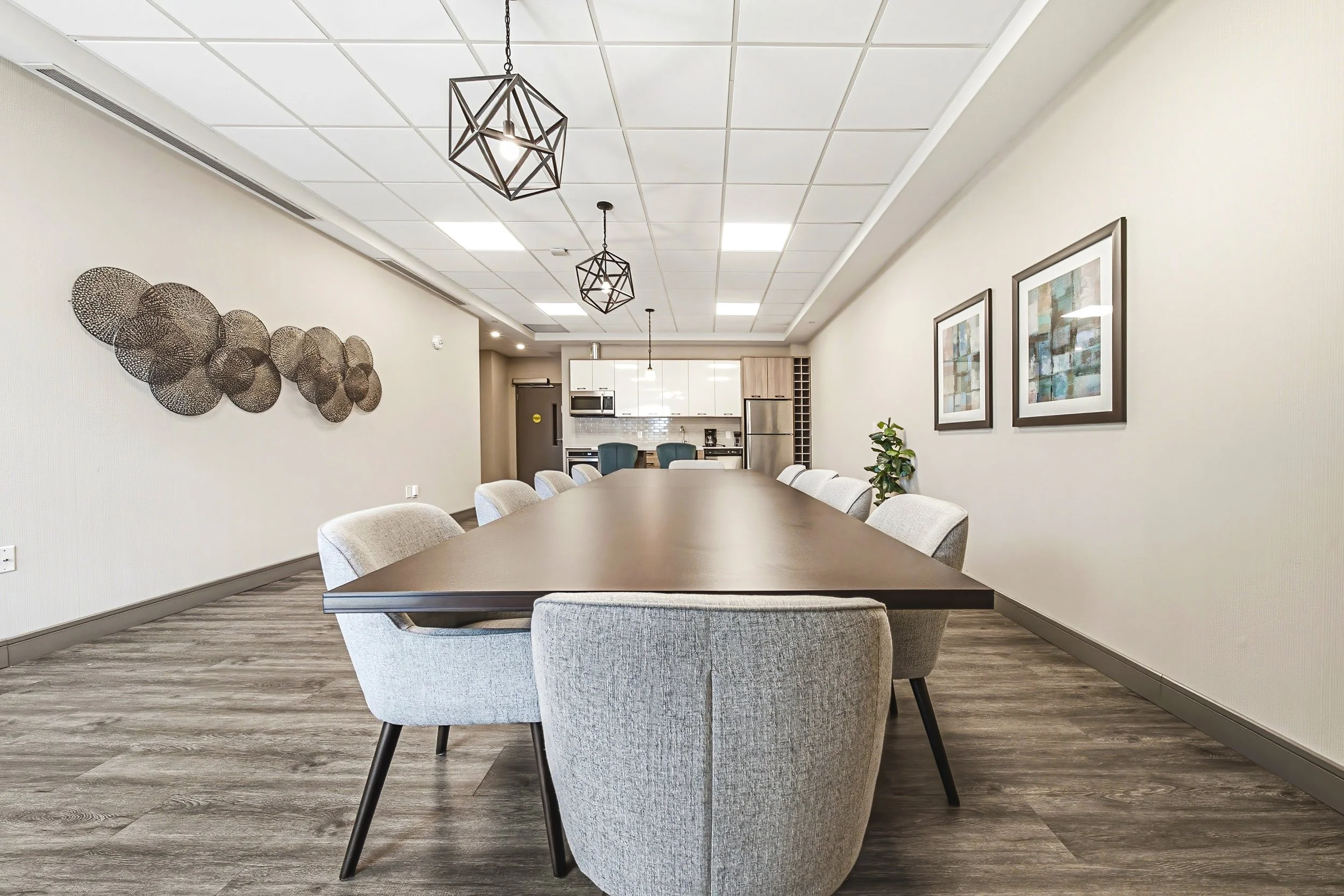 A conference room with a long table surrounded by upholstered chairs, wall art, and hanging geometric pendant lights.