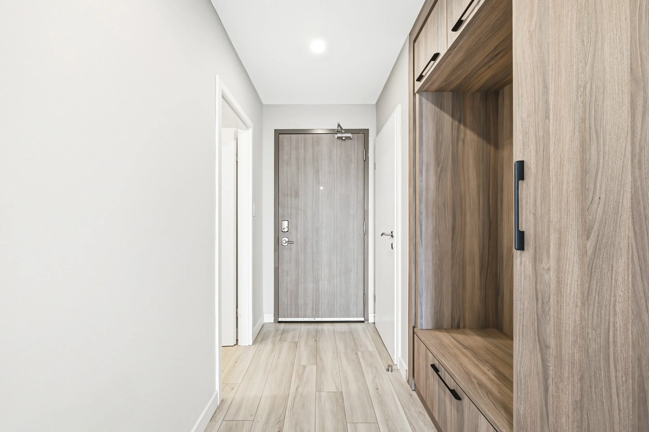 Interior of an entryway with a gray front door, white walls, light wood flooring, and a built-in wooden cabinet on the right side.