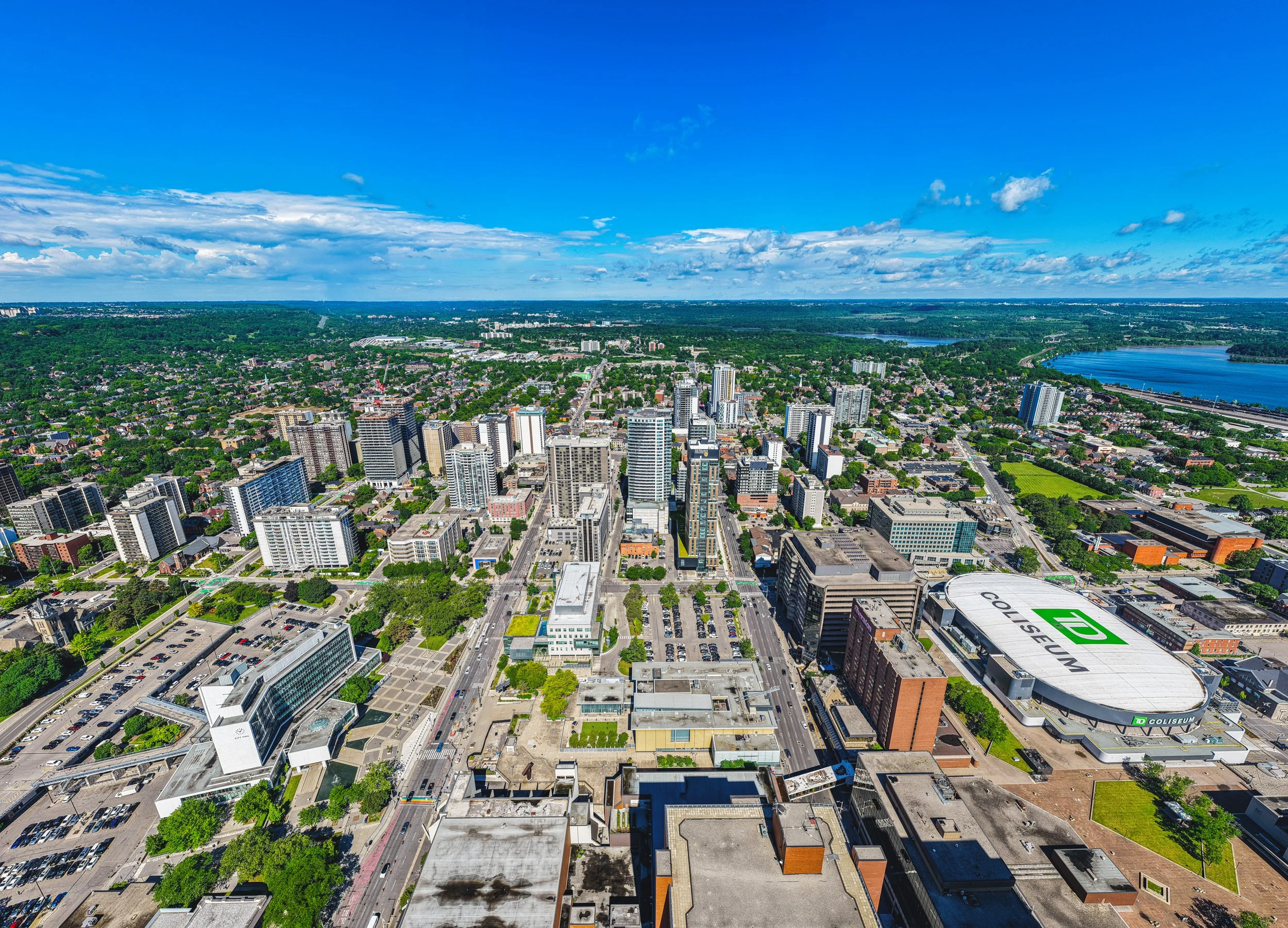 Aerial view of a city with tall buildings, green trees, a river, and a large stadium with a TD logo on the roof.