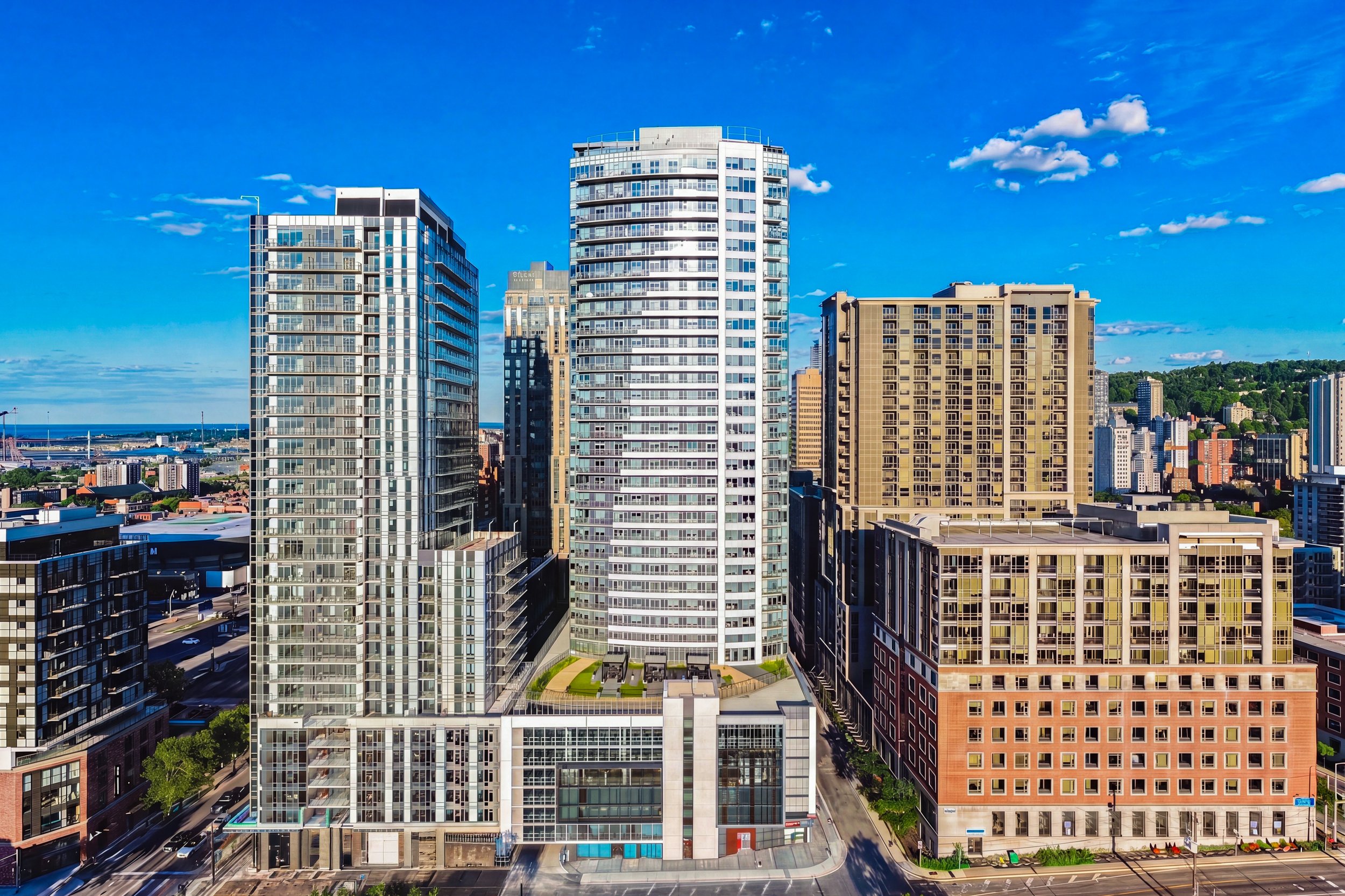 A city skyline with tall modern high-rise buildings under a bright blue sky with scattered clouds.