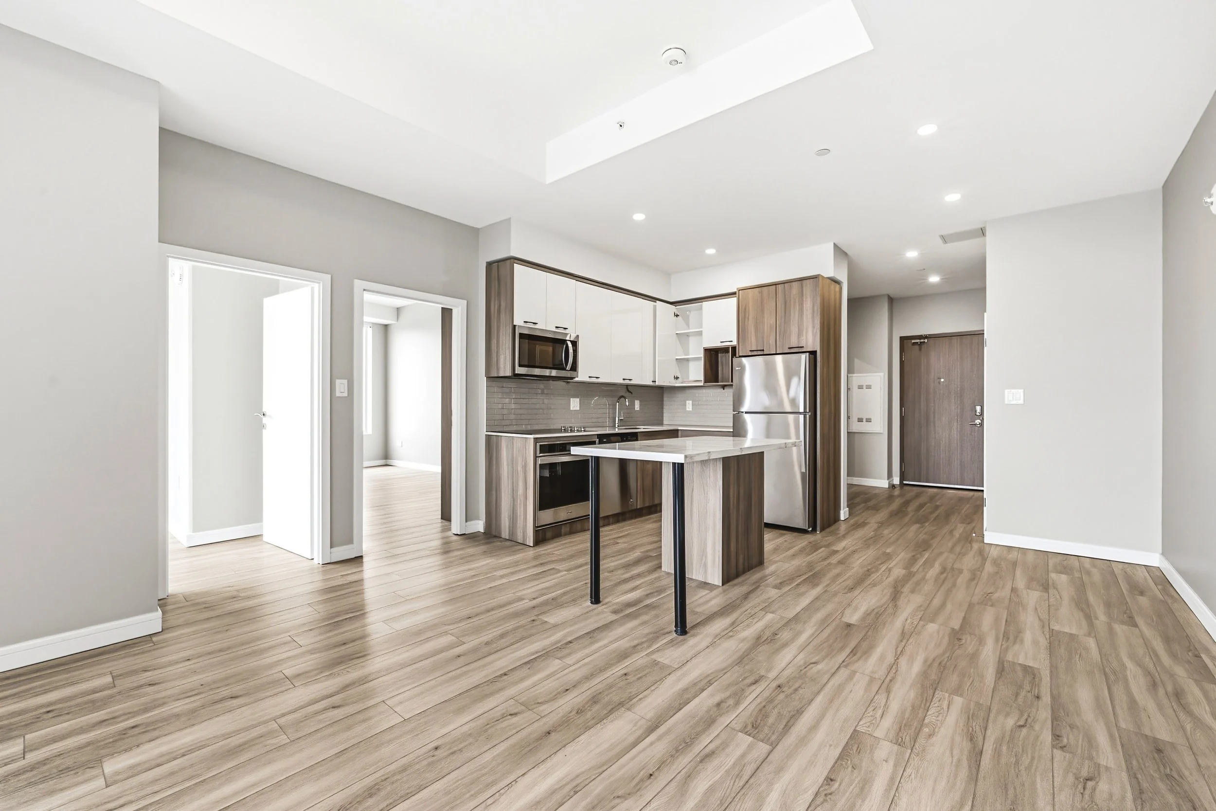 Modern kitchen with wooden flooring, white and wood cabinets, stainless steel appliances, and a small kitchen island.