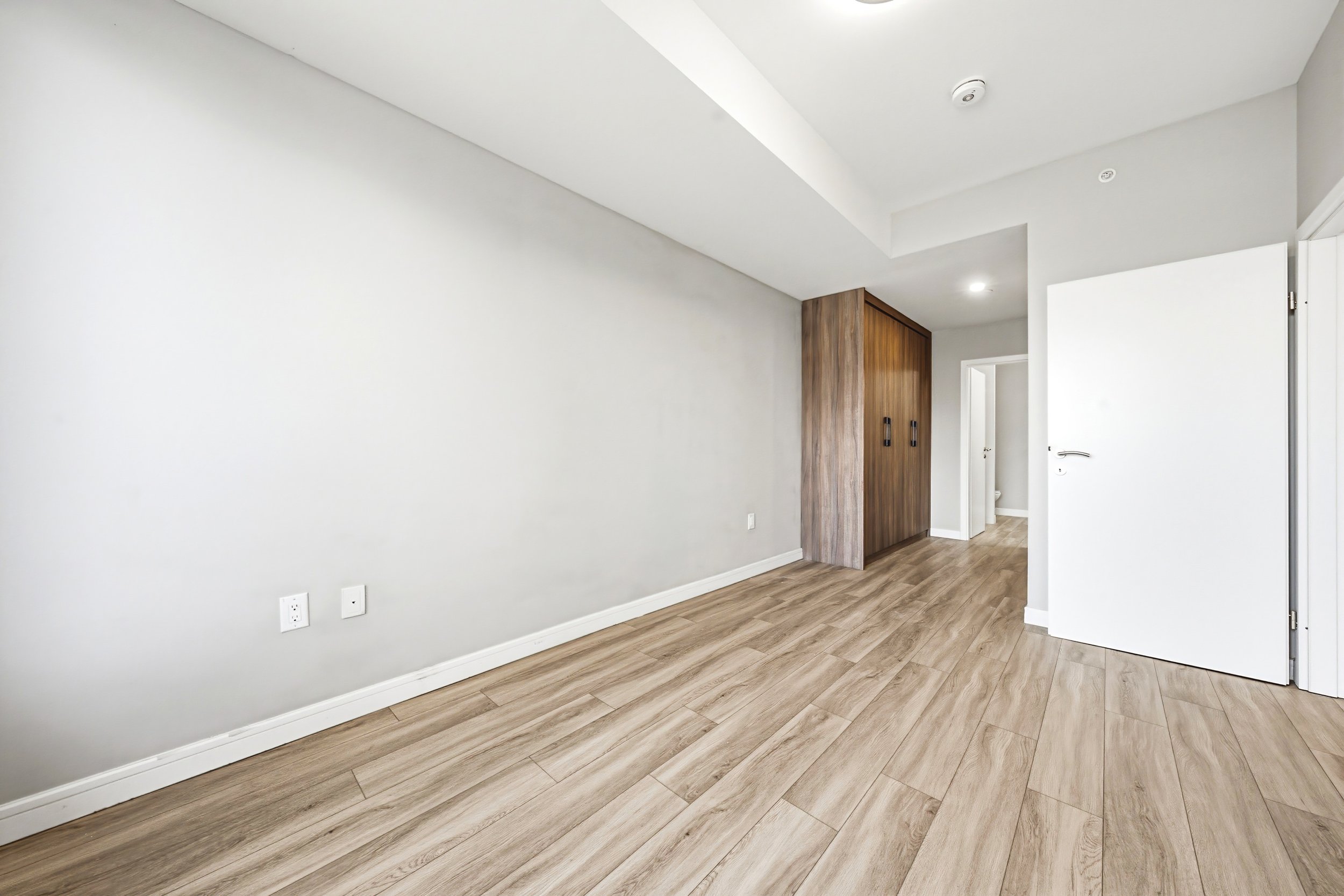 Empty room with light wood flooring, white walls, a wooden closet, and an open door.