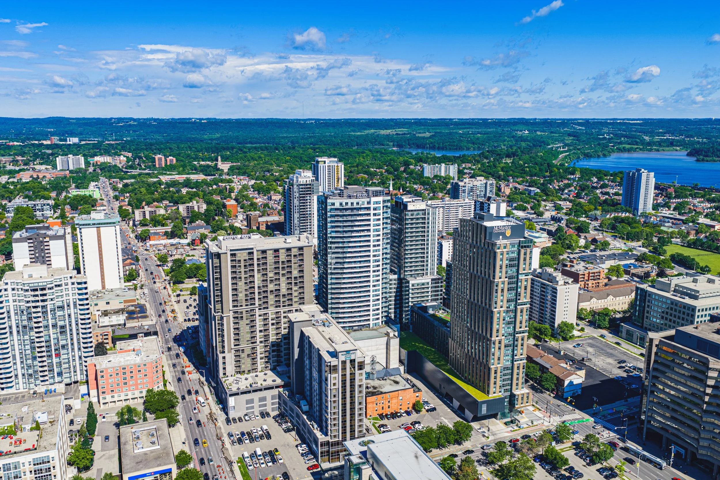 A cityscape with tall modern buildings, a park with trees, a lake, and a partly cloudy sky.
