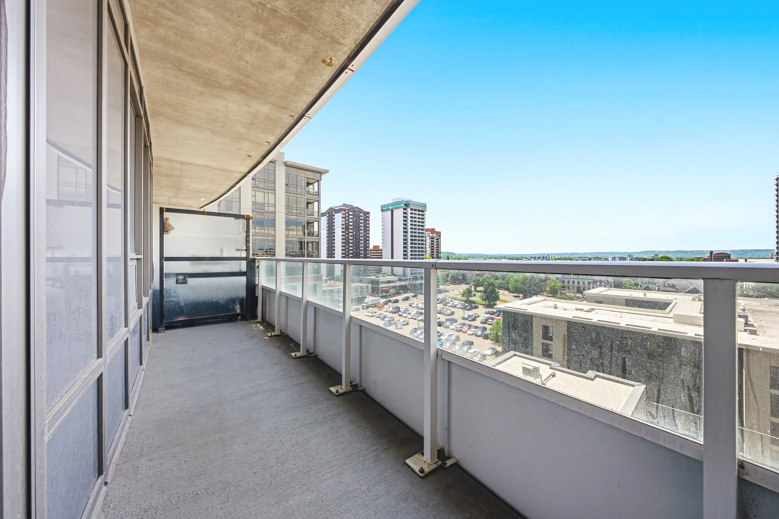 View from a balcony showing a cityscape with several high-rise buildings, parking lots, and a clear blue sky.