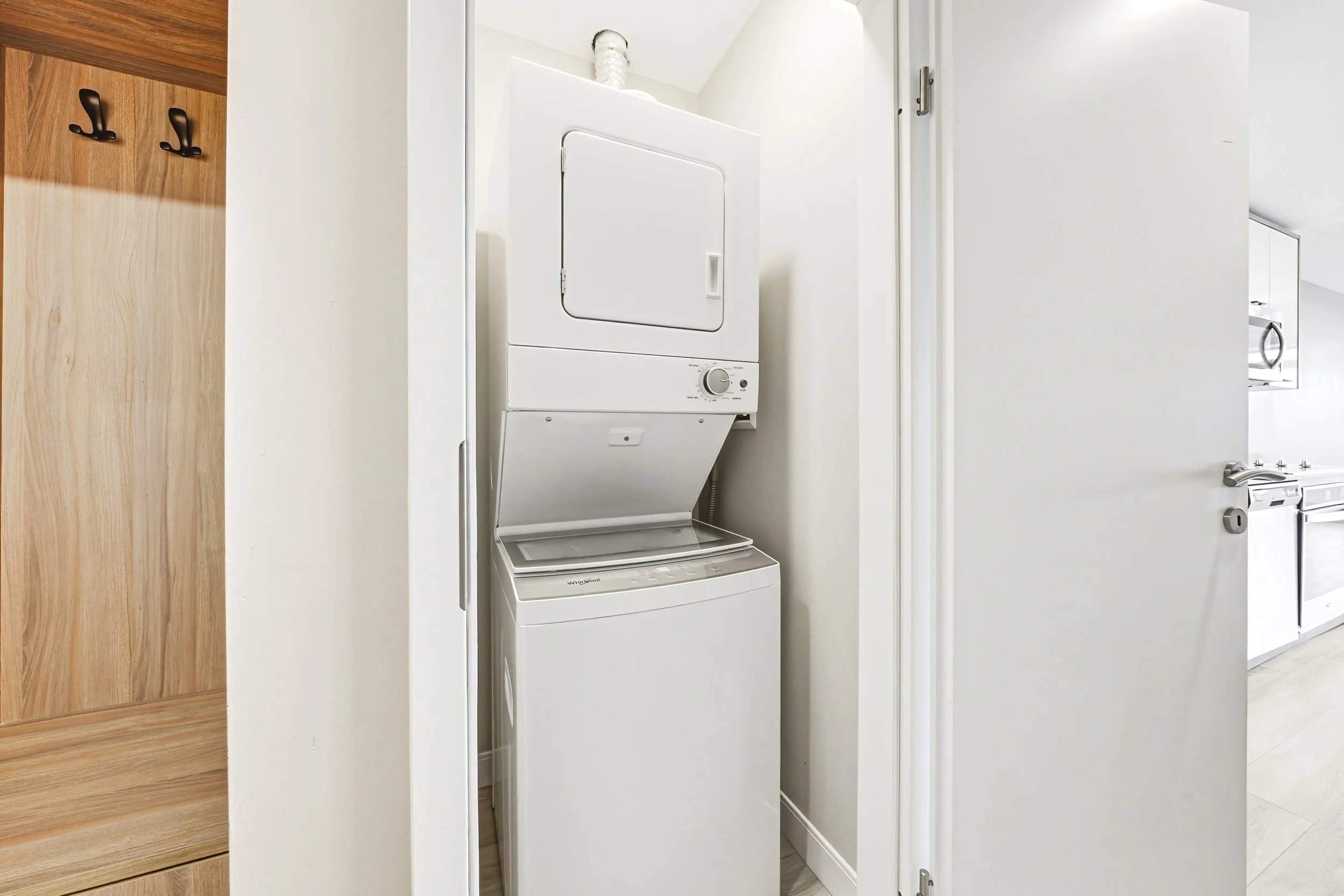 Laundry area with a stacked washer and dryer behind a white door, with a wooden surface on the left side.