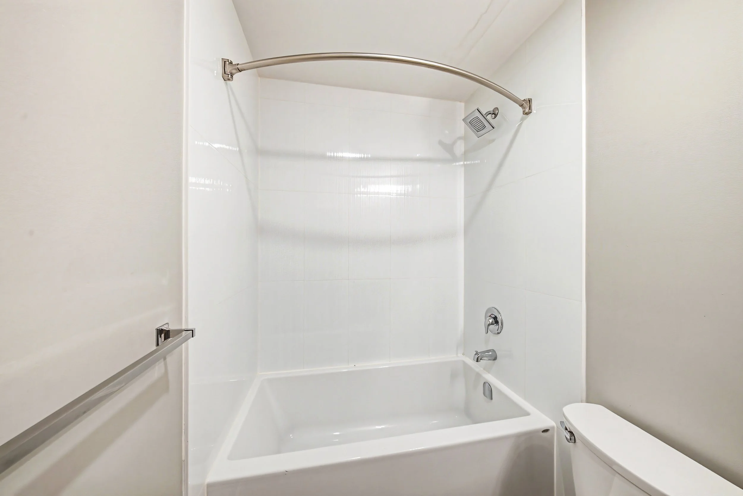 A white bathtub with a showerhead, soap dish, and a bar of soap. There is a grab bar on the wall, and a toilet is partly visible beside the tub.