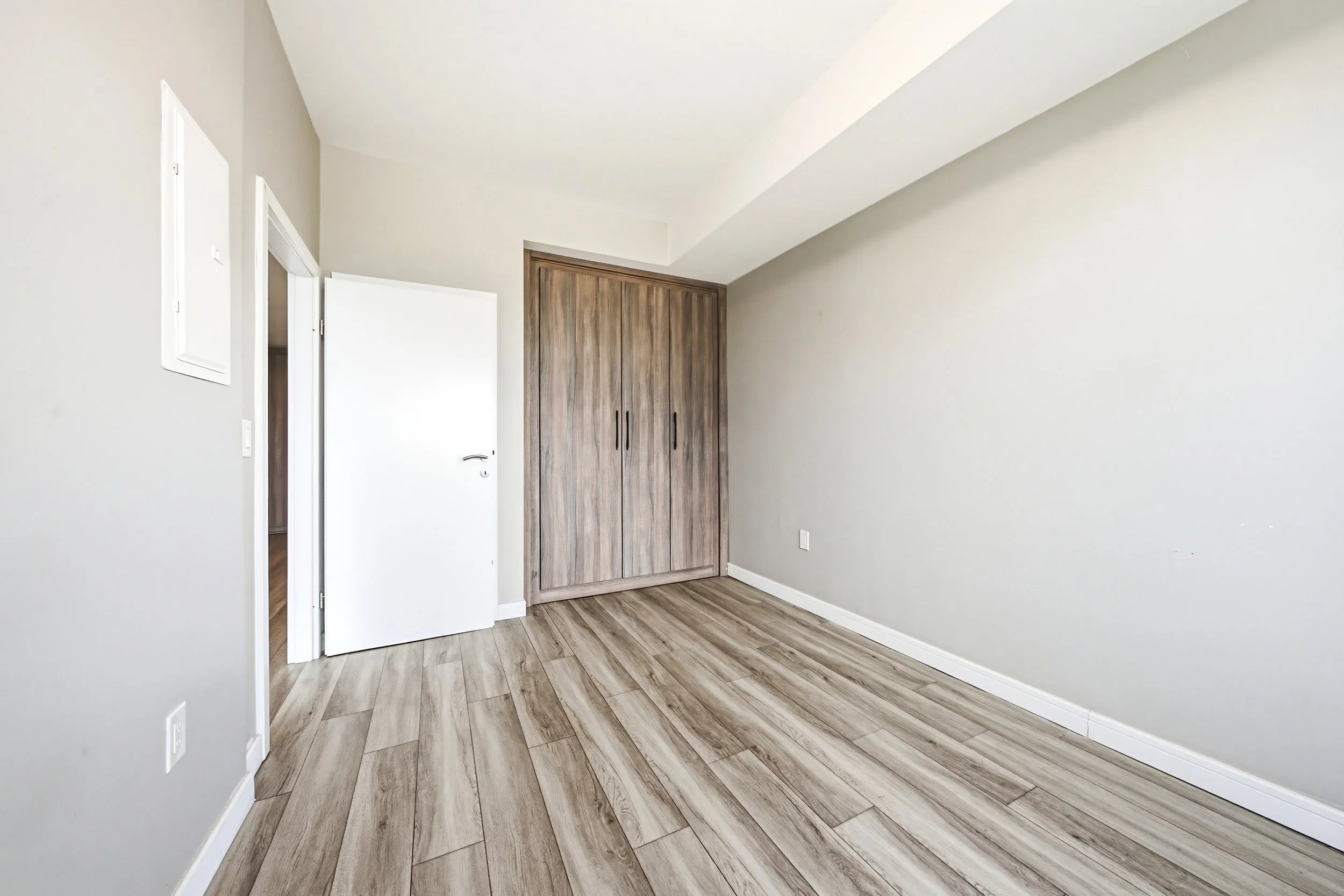 Empty room with light-colored walls, wooden closet doors, ceiling sloped at an angle, hardwood flooring, and a partially open door.