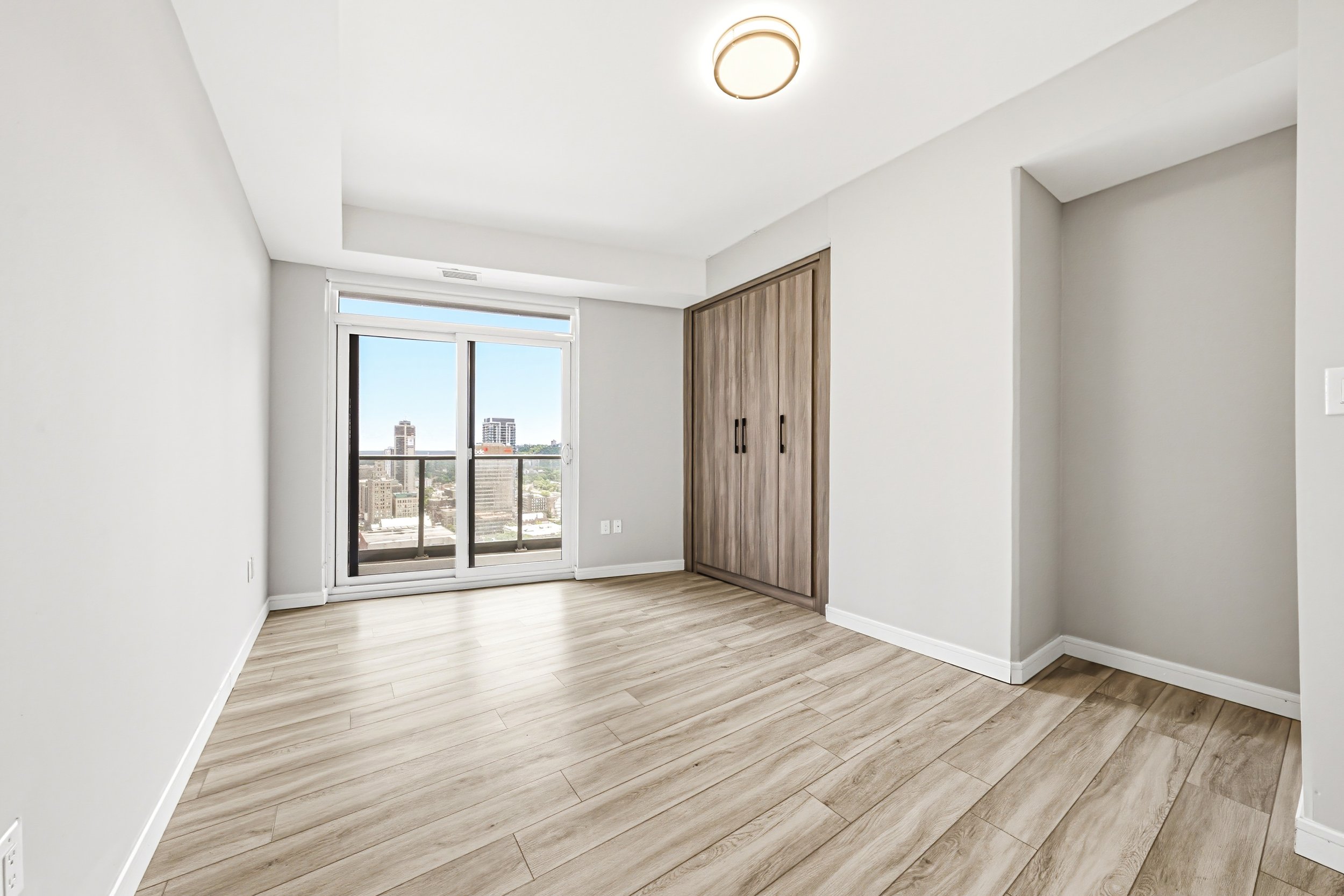 Empty room with white walls, wood flooring, sliding glass door leading to a balcony, and built-in wooden closet.