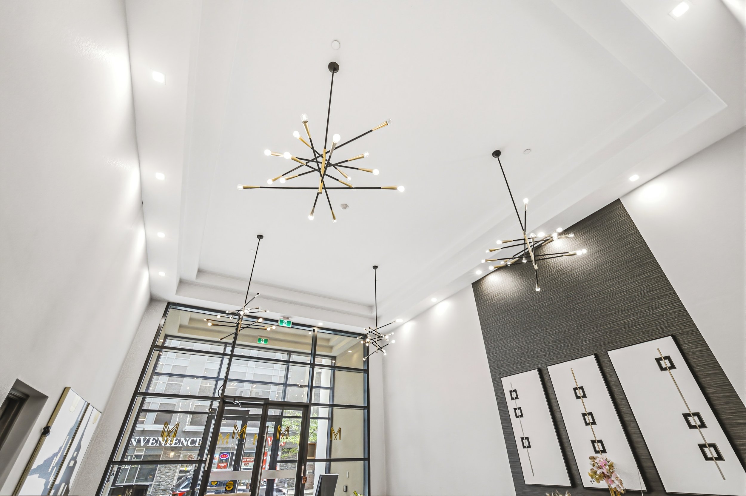 Modern lobby area with white walls, large glass doors, and unique black and gold chandeliers hanging from the ceiling.
