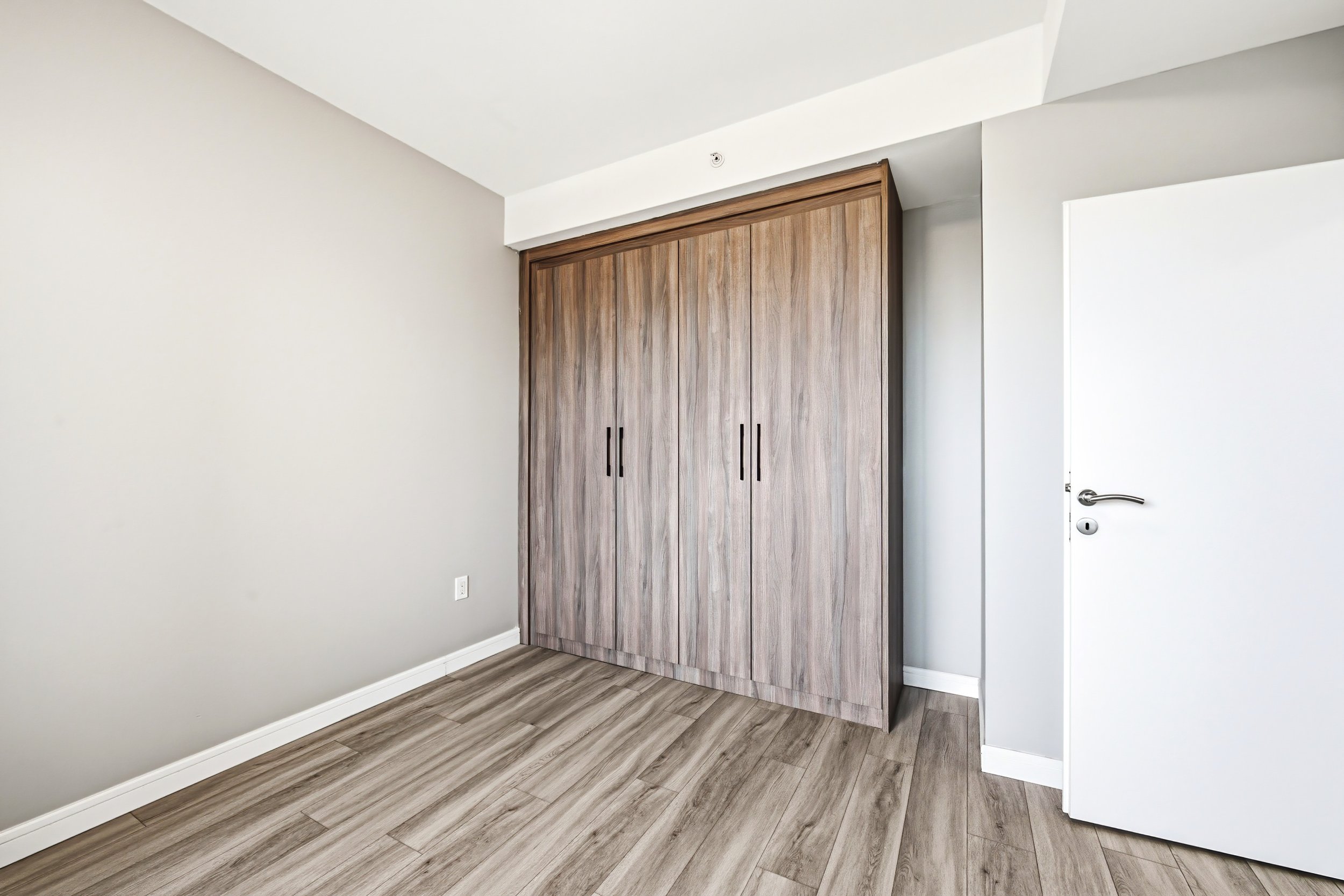 A minimalist room with a wooden closet and a white door, beige walls, and wood laminate flooring.
