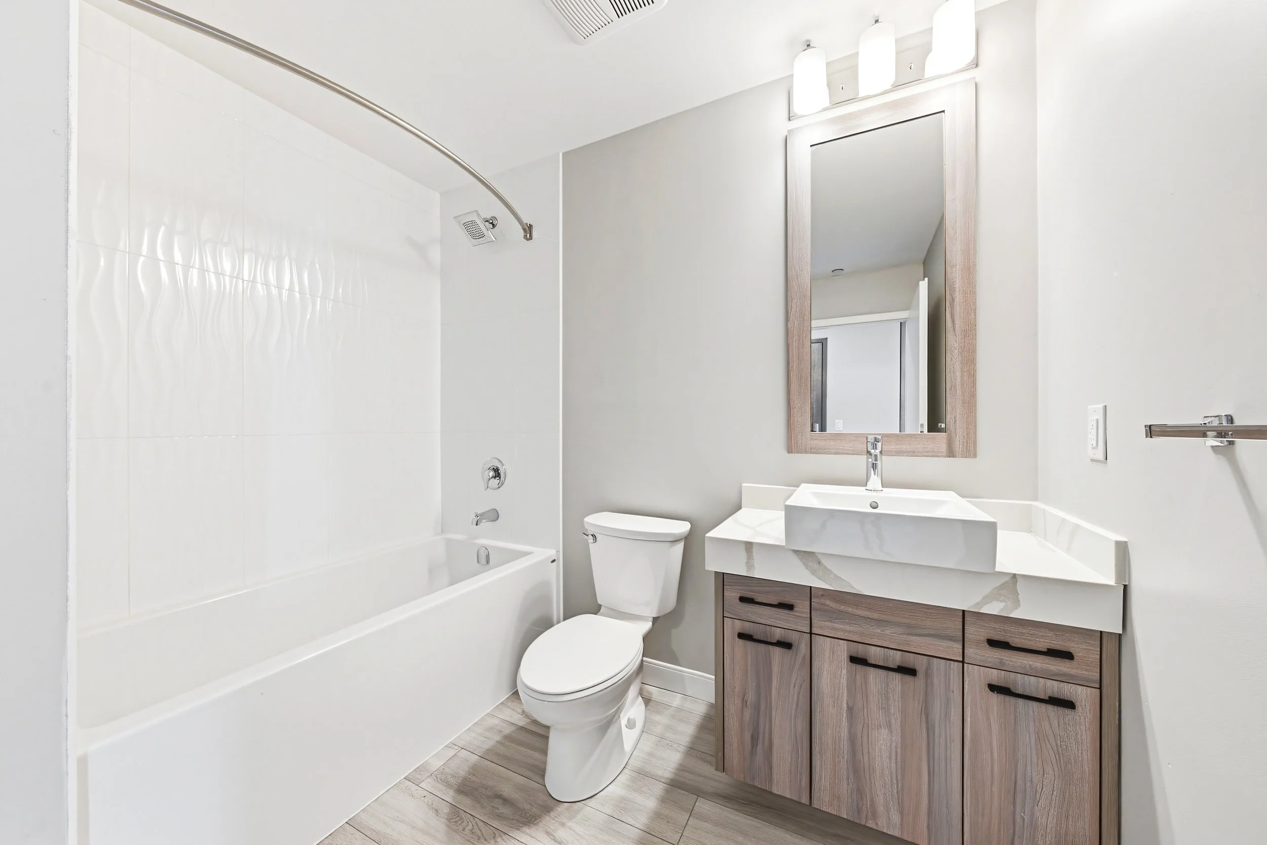 Modern bathroom with a bathtub and shower, toilet, and vanity with sink, mirror, and lighting fixtures.