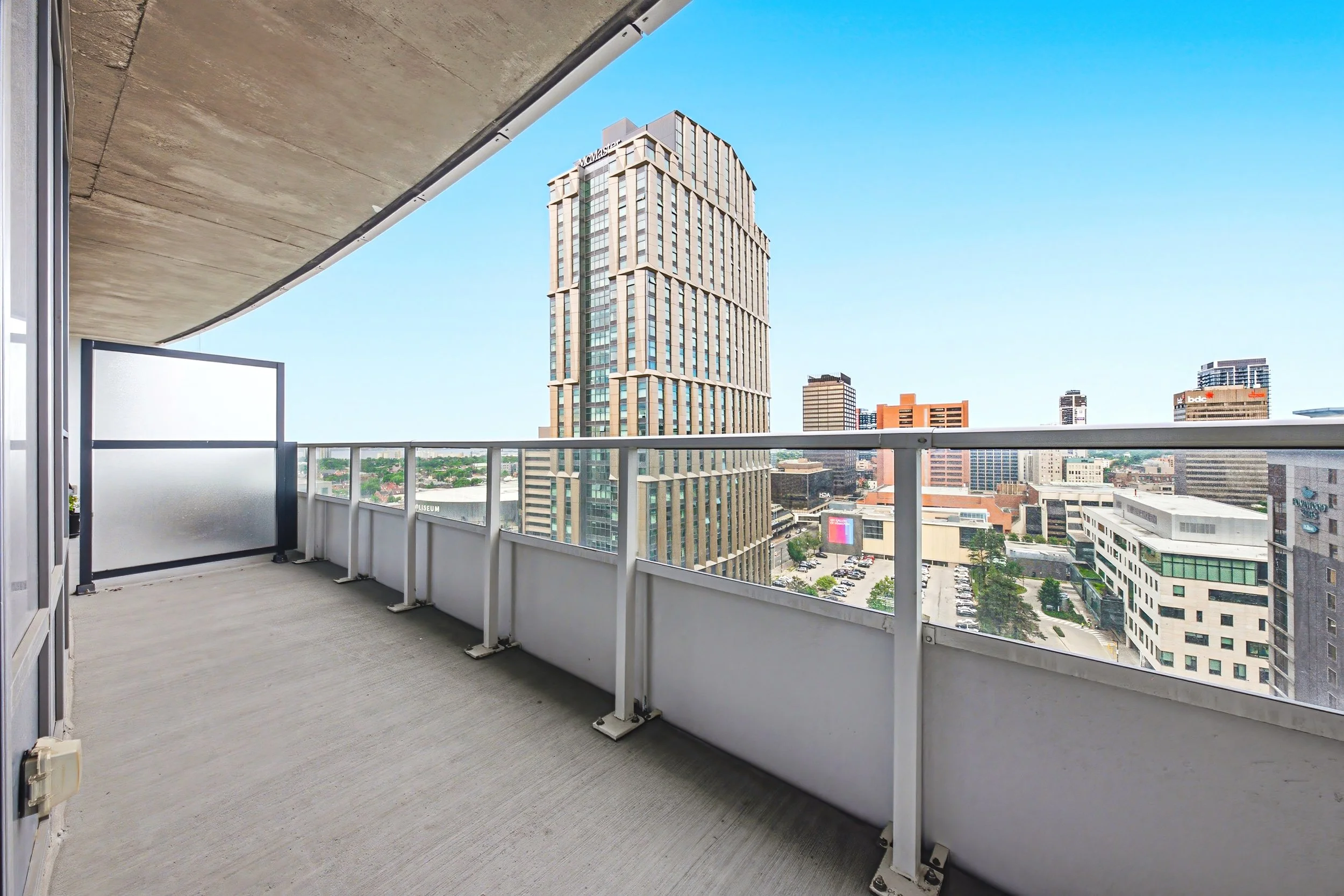 Balcony with view of city skyscrapers and blue sky, with frosted glass panels on the railing.