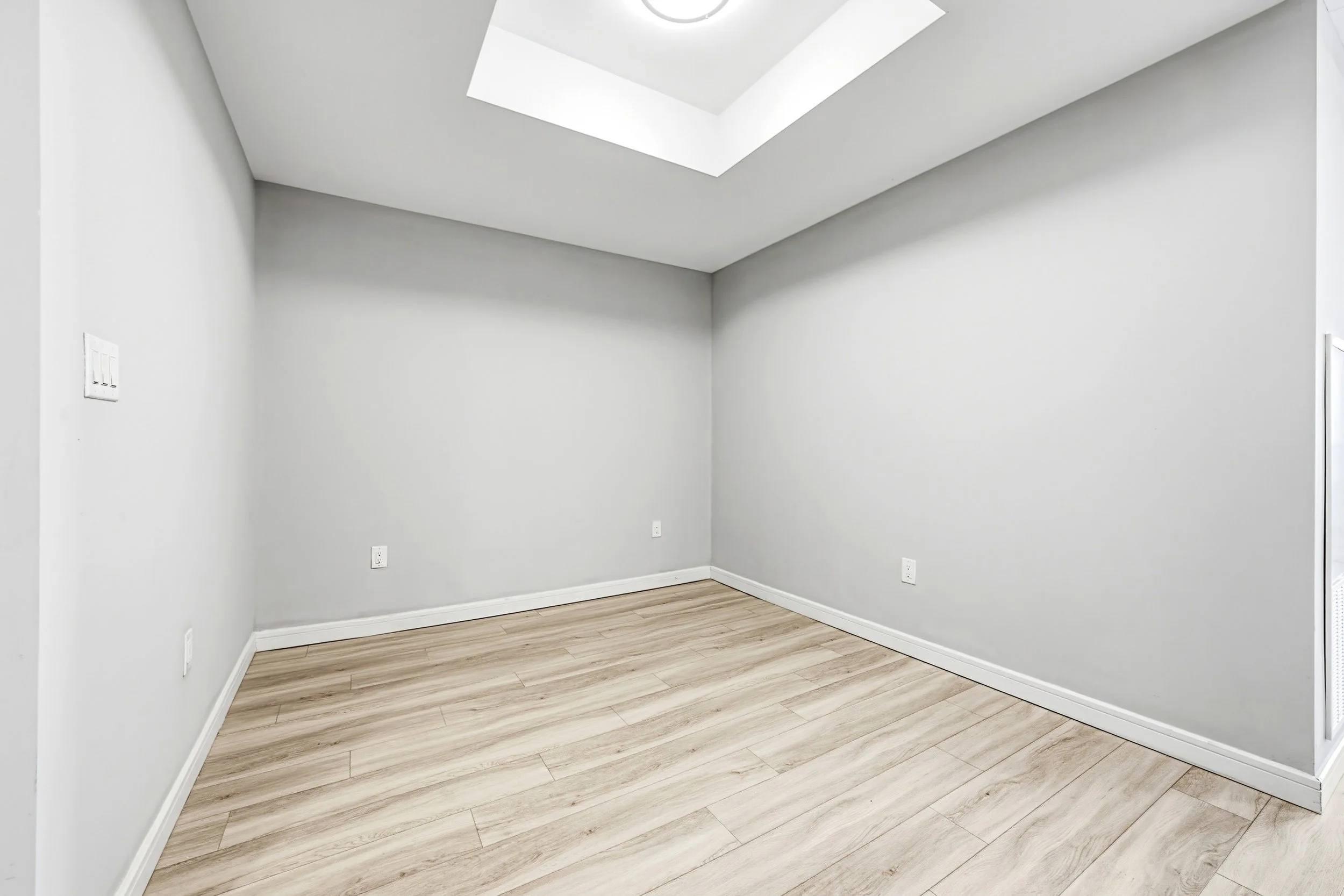 Empty room with light gray walls, ceiling, and wood flooring.