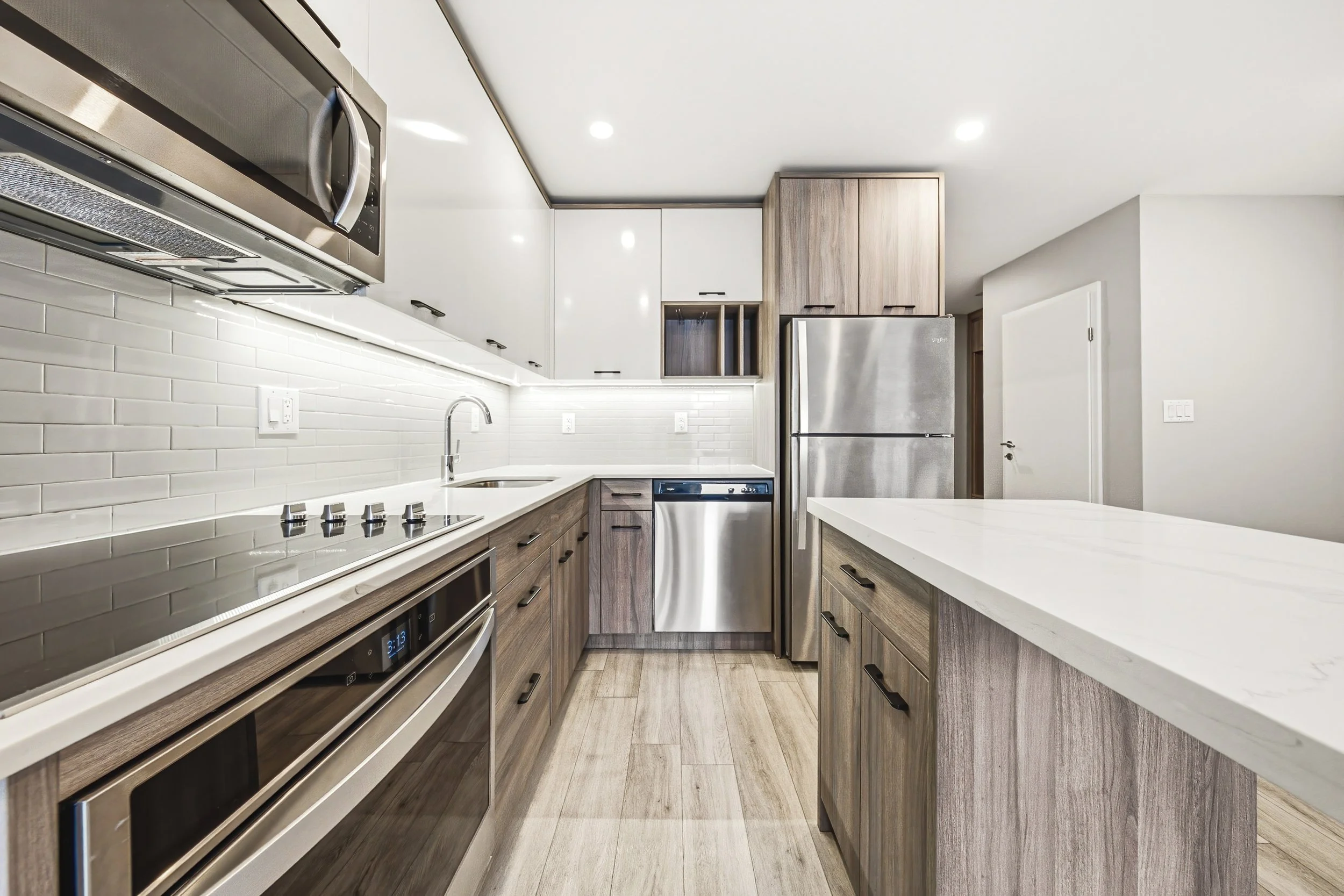 Modern kitchen with white backsplash, wooden cabinets, stainless steel appliances, and a white countertop.
