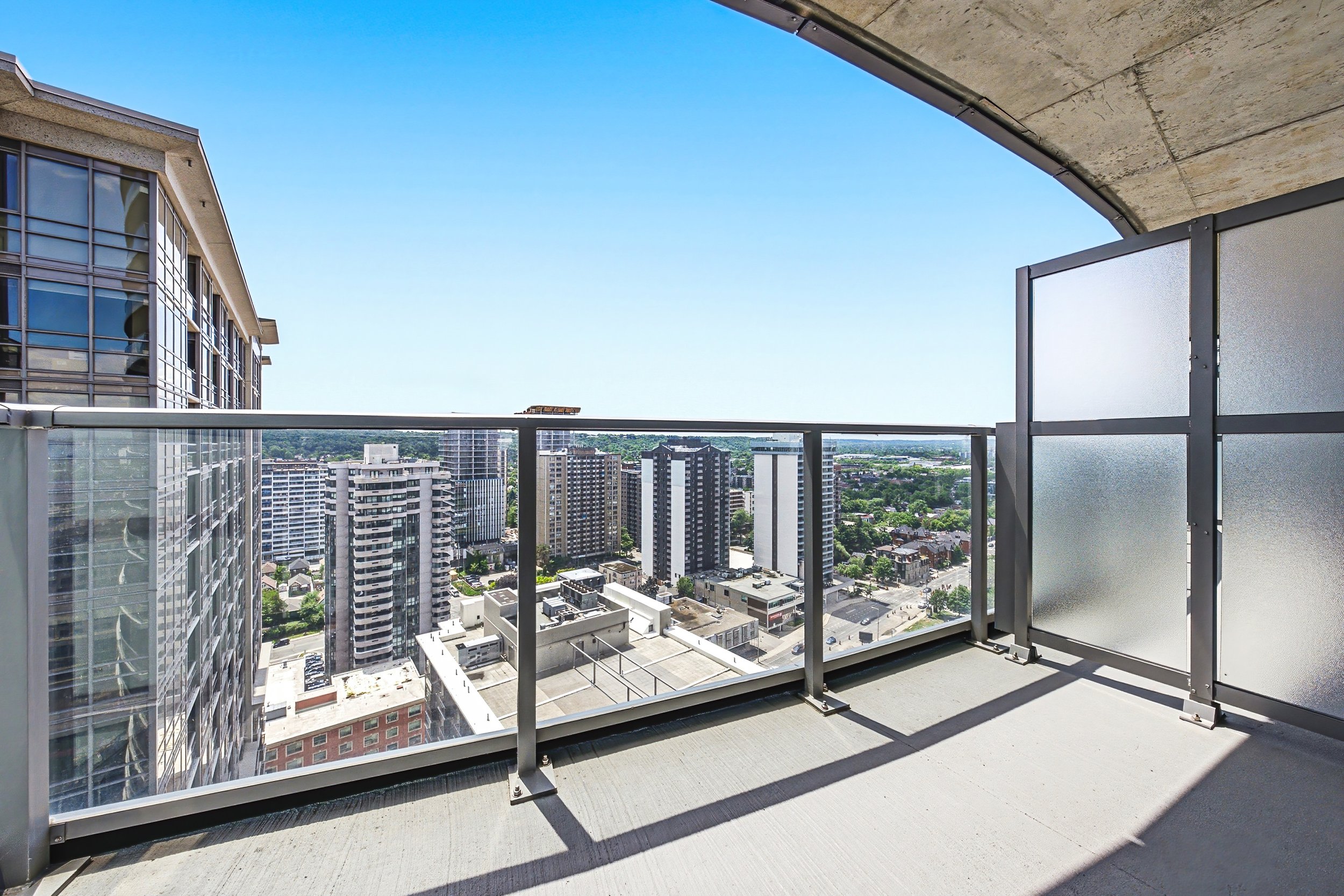 Balcony with metal railing overlooking a cityscape of high-rise buildings under a clear blue sky.