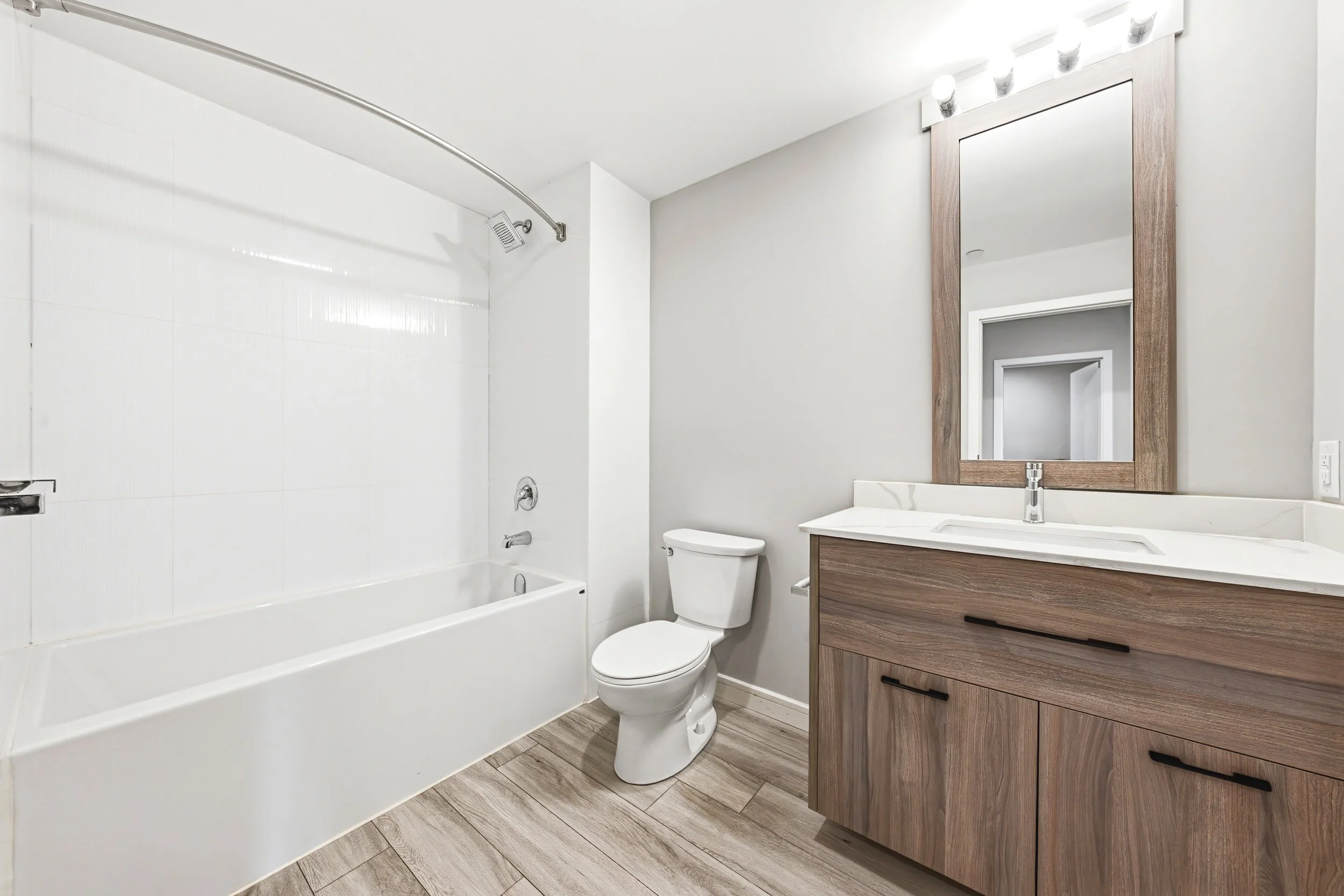Modern bathroom with a bathtub and shower, white toilet, wooden vanity with a sink, large mirror, and a light fixture above the mirror.