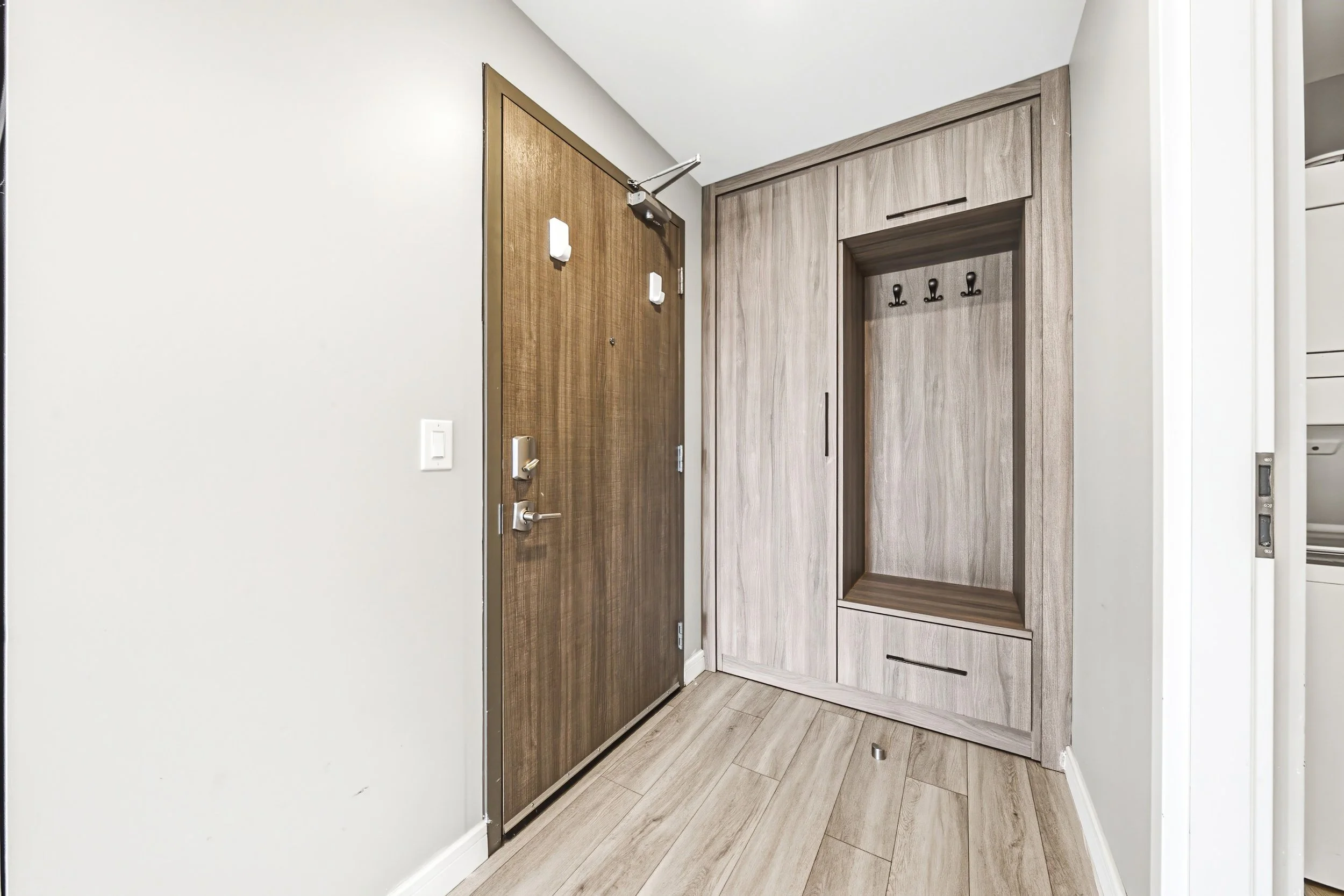 Entryway with a wooden door, a built-in wooden closet with hooks, and light-colored wood flooring.