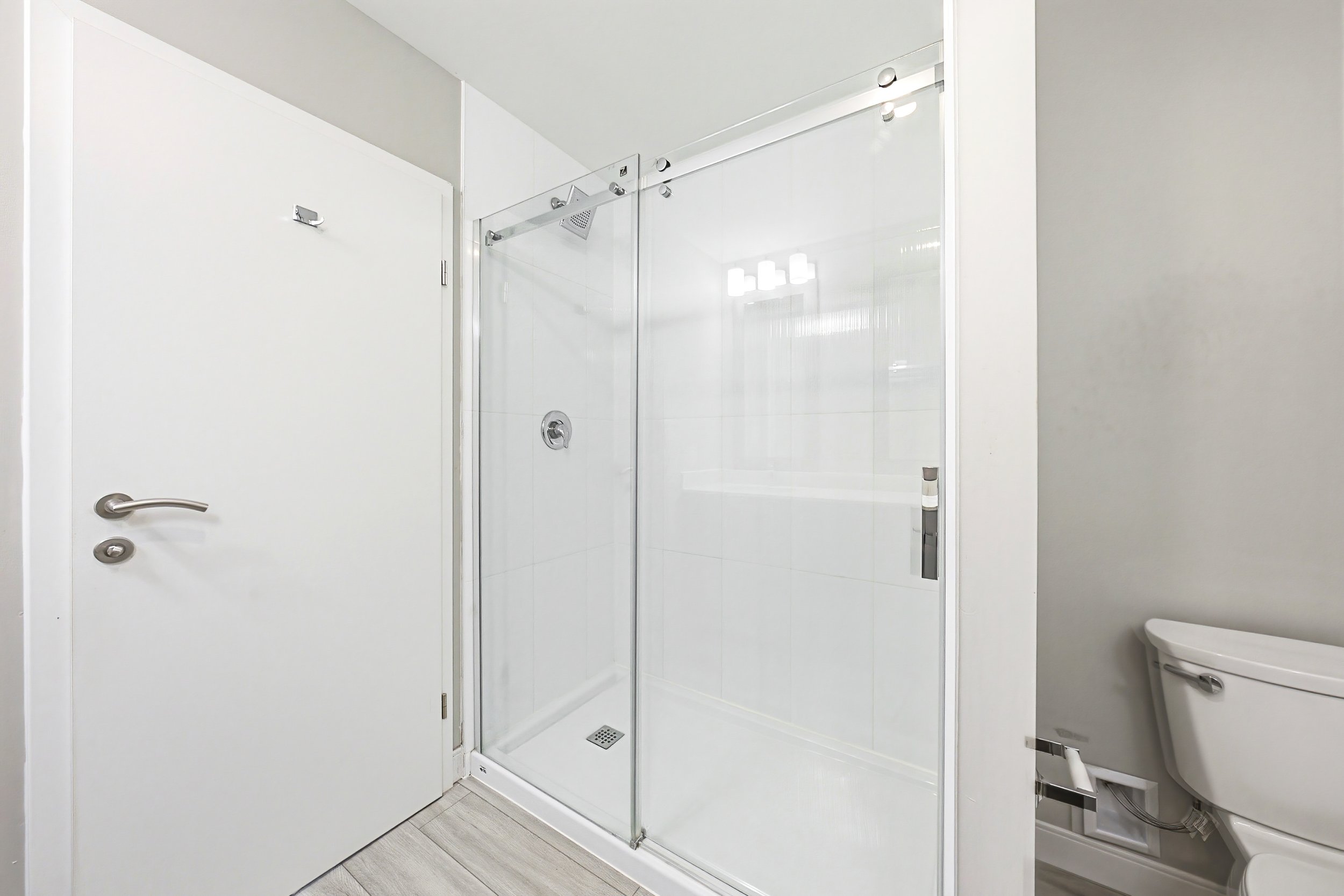 Modern bathroom with a glass-enclosed shower, white interior, and visible fixtures including a door handle and a toilet.