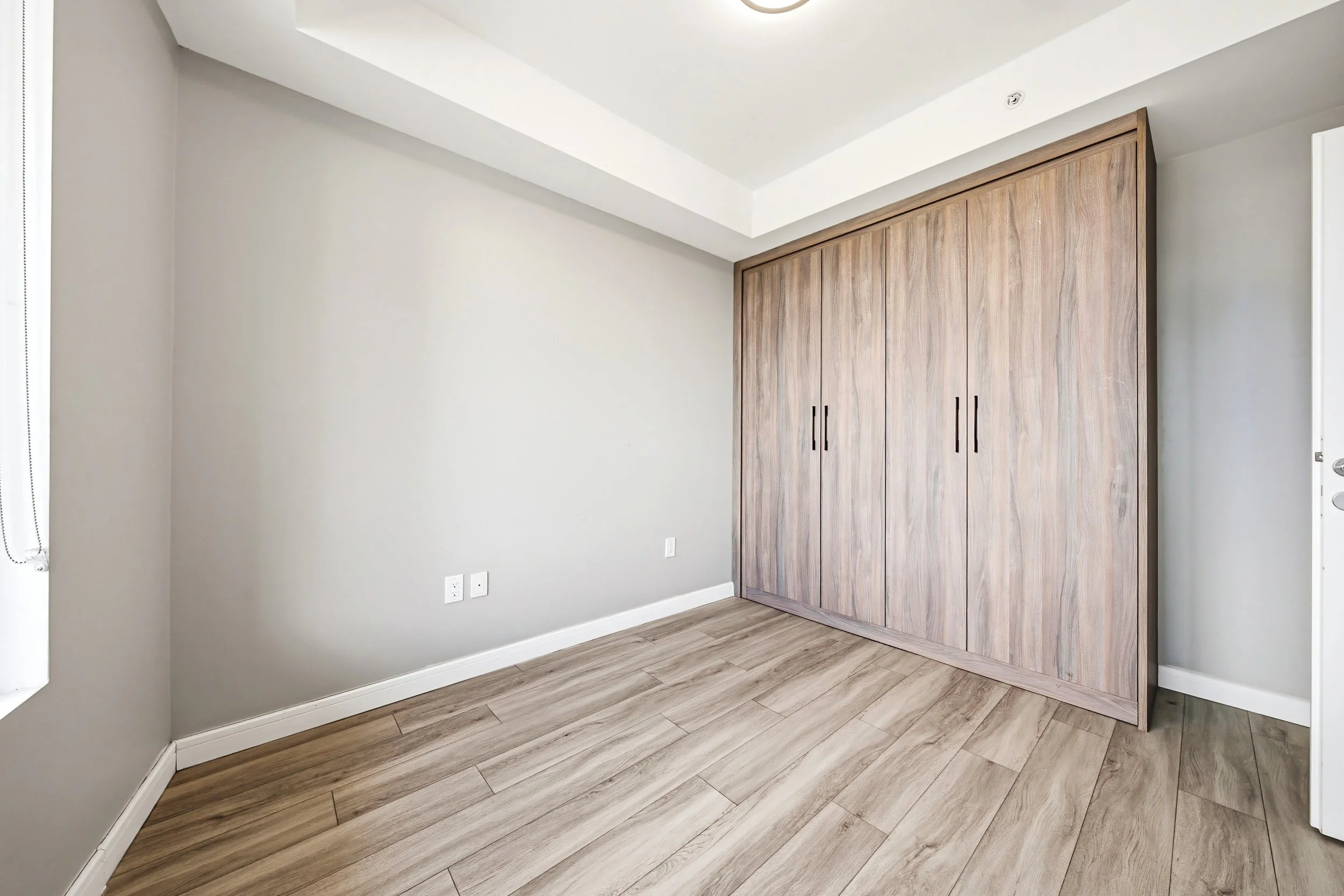 Empty room with gray walls, a large wooden closet, and light wood flooring.