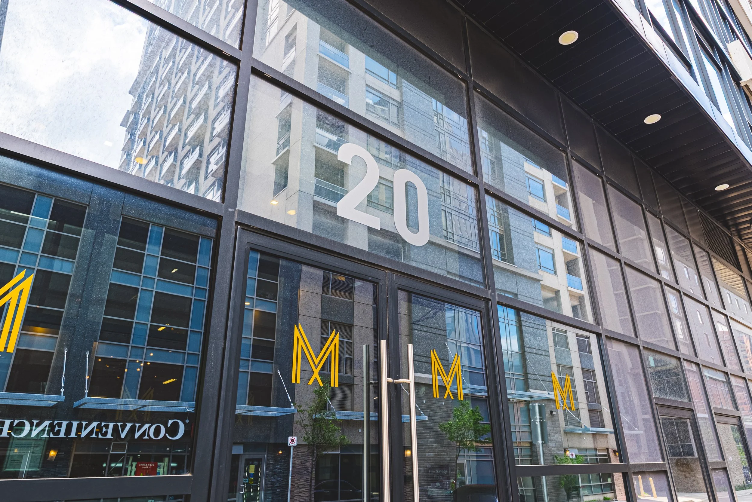 View of a modern glass building with the number '120'. Reflection of surrounding buildings and the street can be seen in the glass.