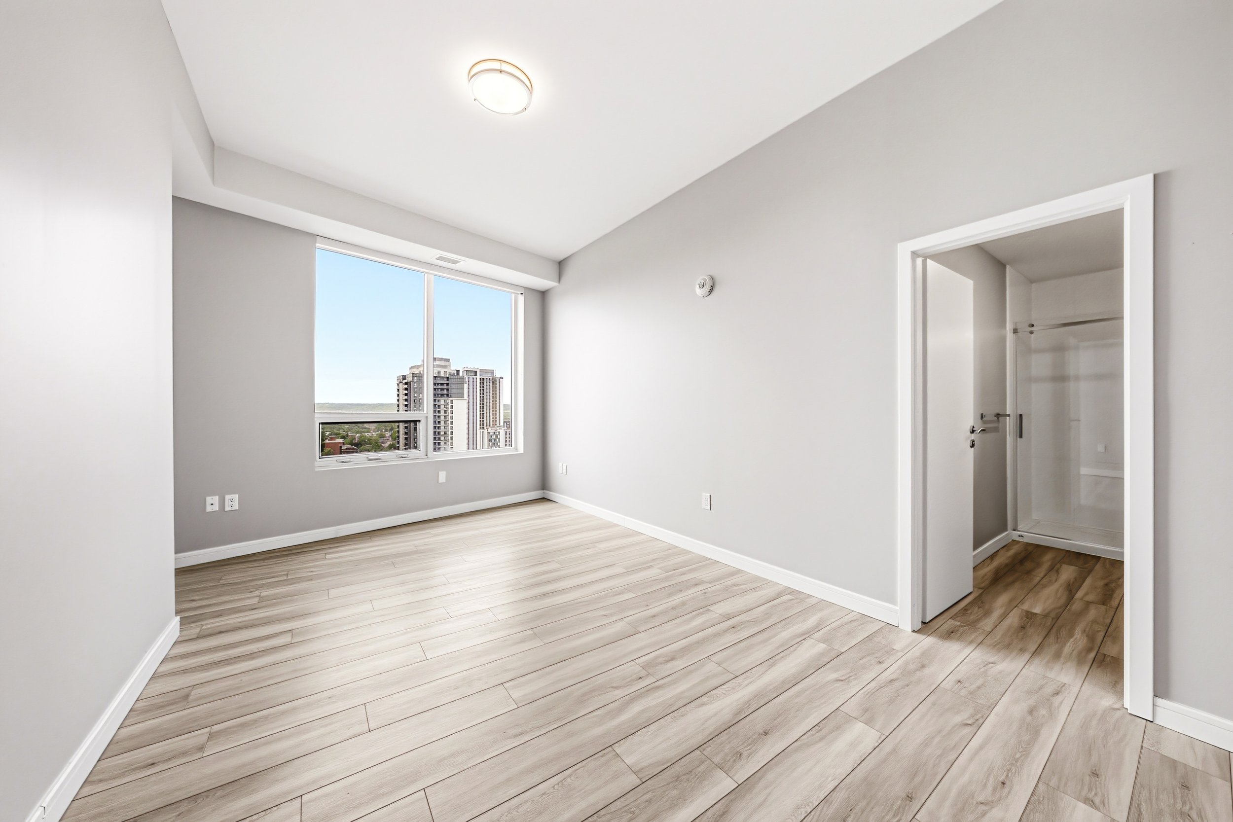 Empty room with large window, white walls, wood flooring, and a closet with an open door.