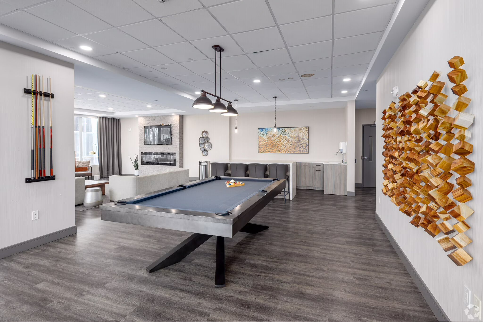 Interior of a modern recreation room featuring a pool table, artwork on the walls, a seating area, and decorative wooden cylindrical sculptures.