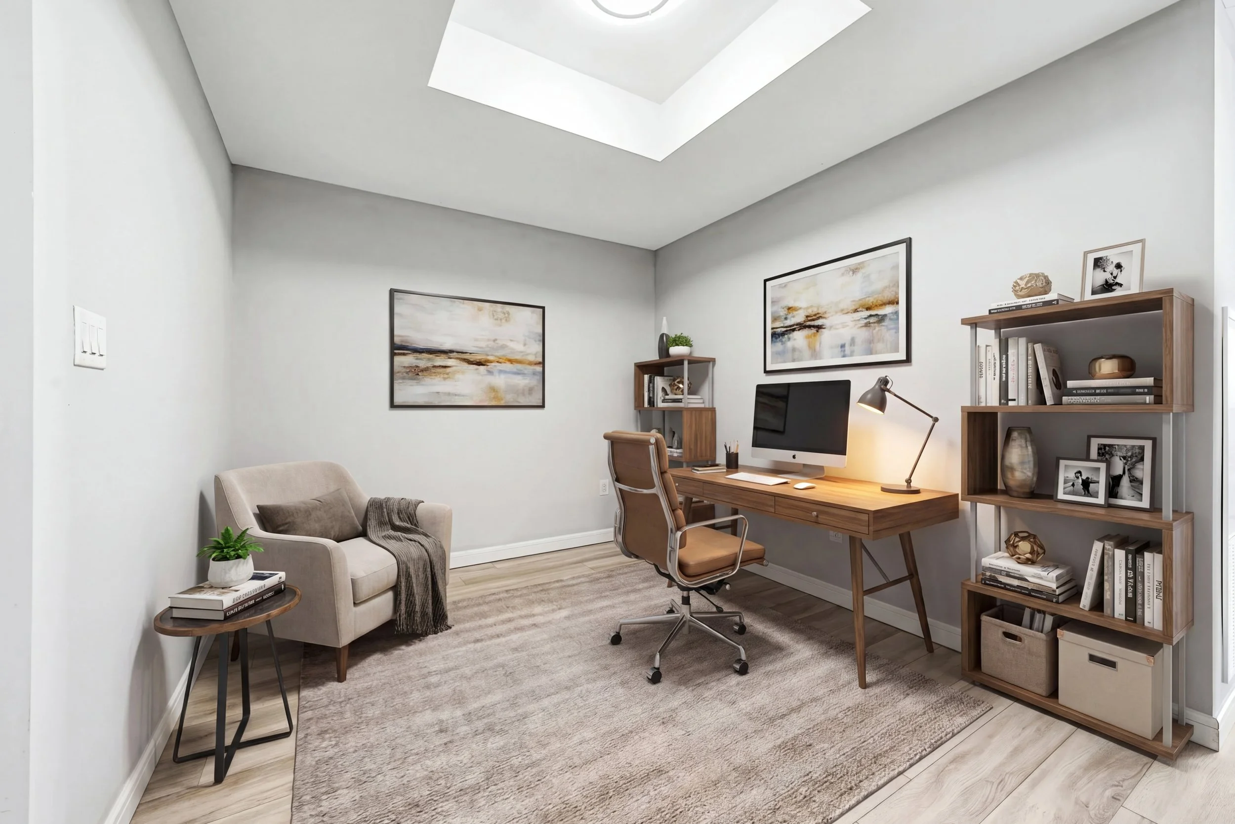 A cozy home office with a beige armchair and a side table on a light-colored wood floor, a gray area rug, a wooden desk with an iMac, a brown office chair, and a wooden bookshelf with framed photos and books, accented with wall art and a small plant.