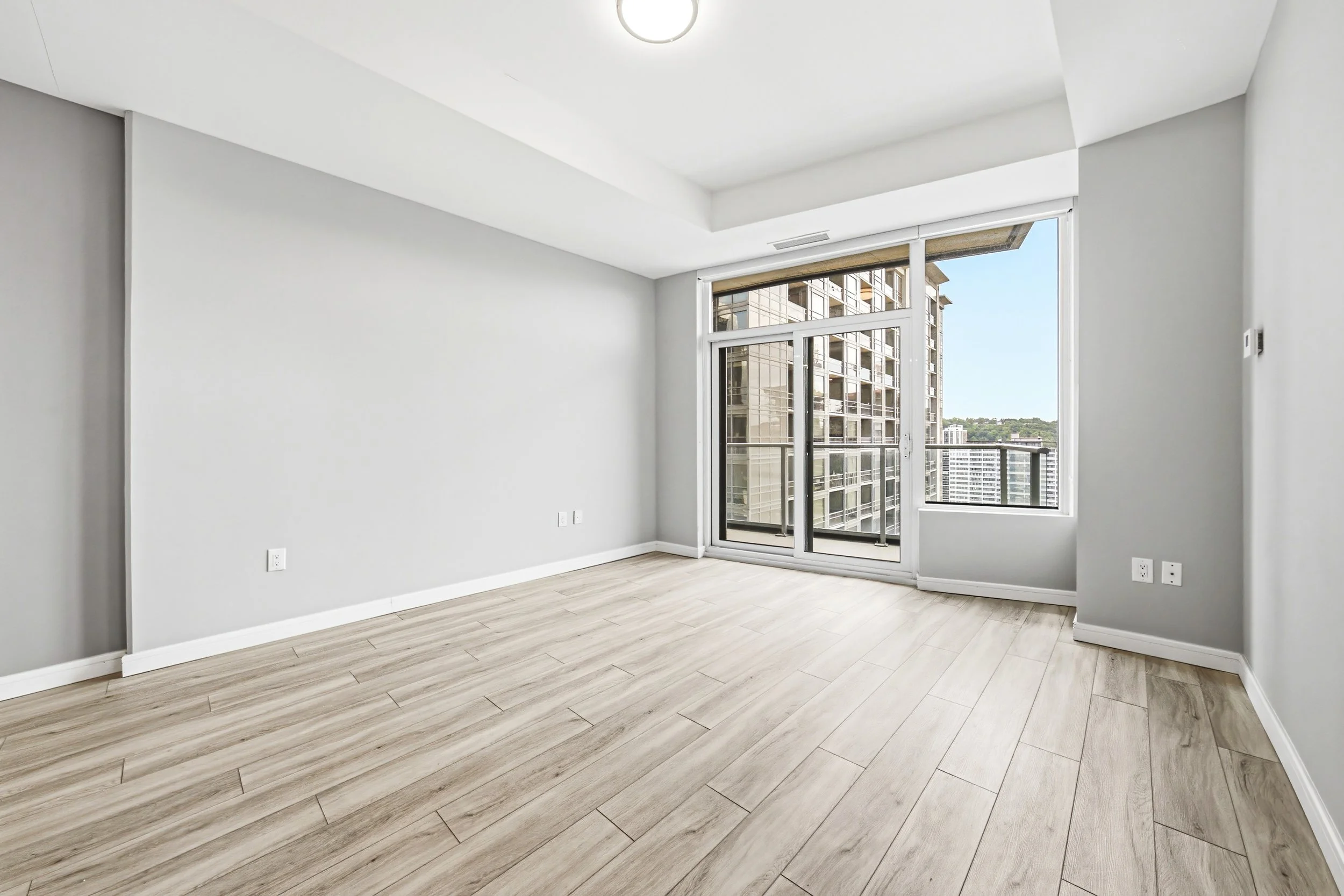 Empty modern apartment room with large windows and light wood flooring.