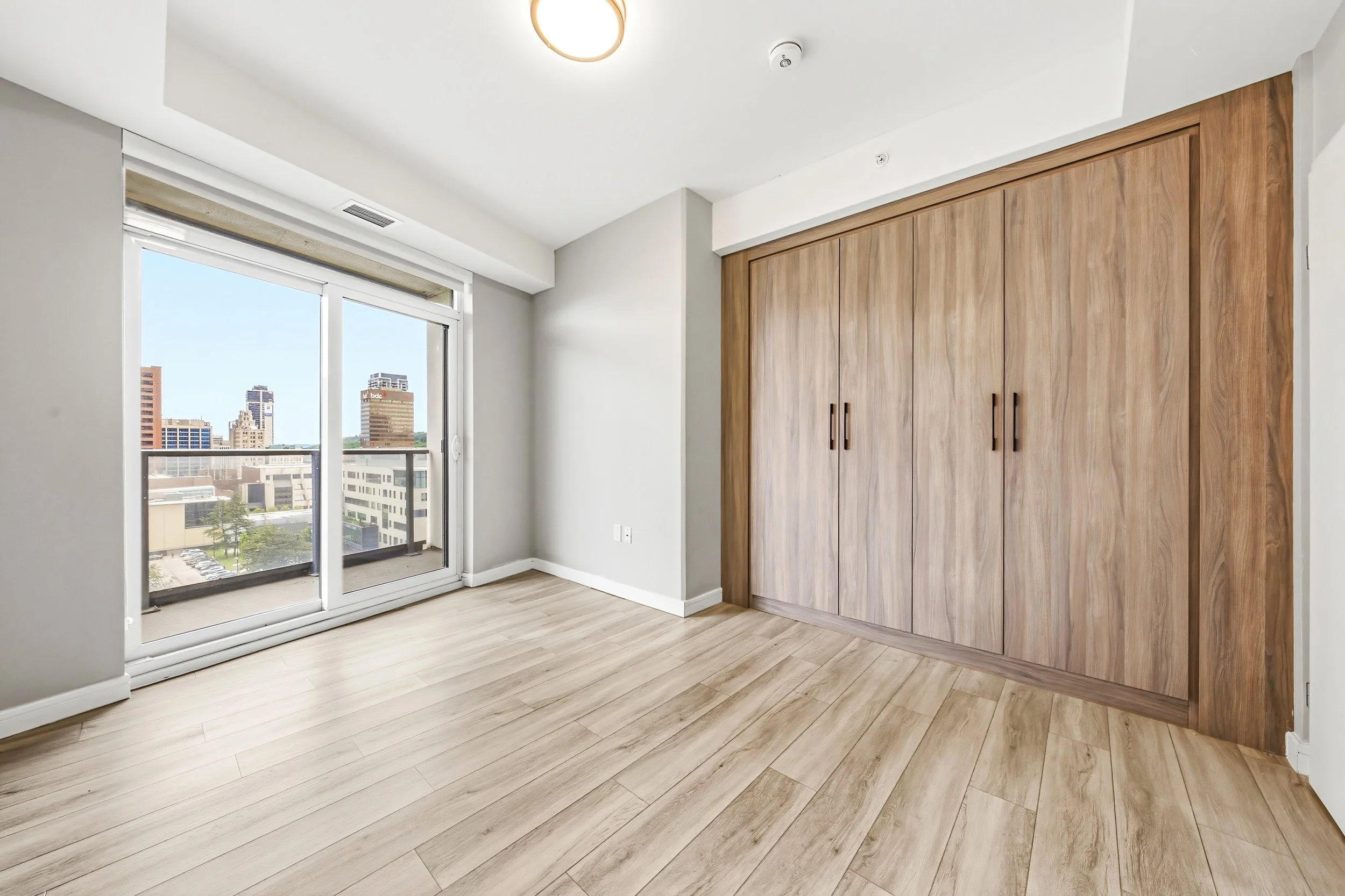 Empty room with wood flooring, a large window with a city view, and a built-in wooden closet.