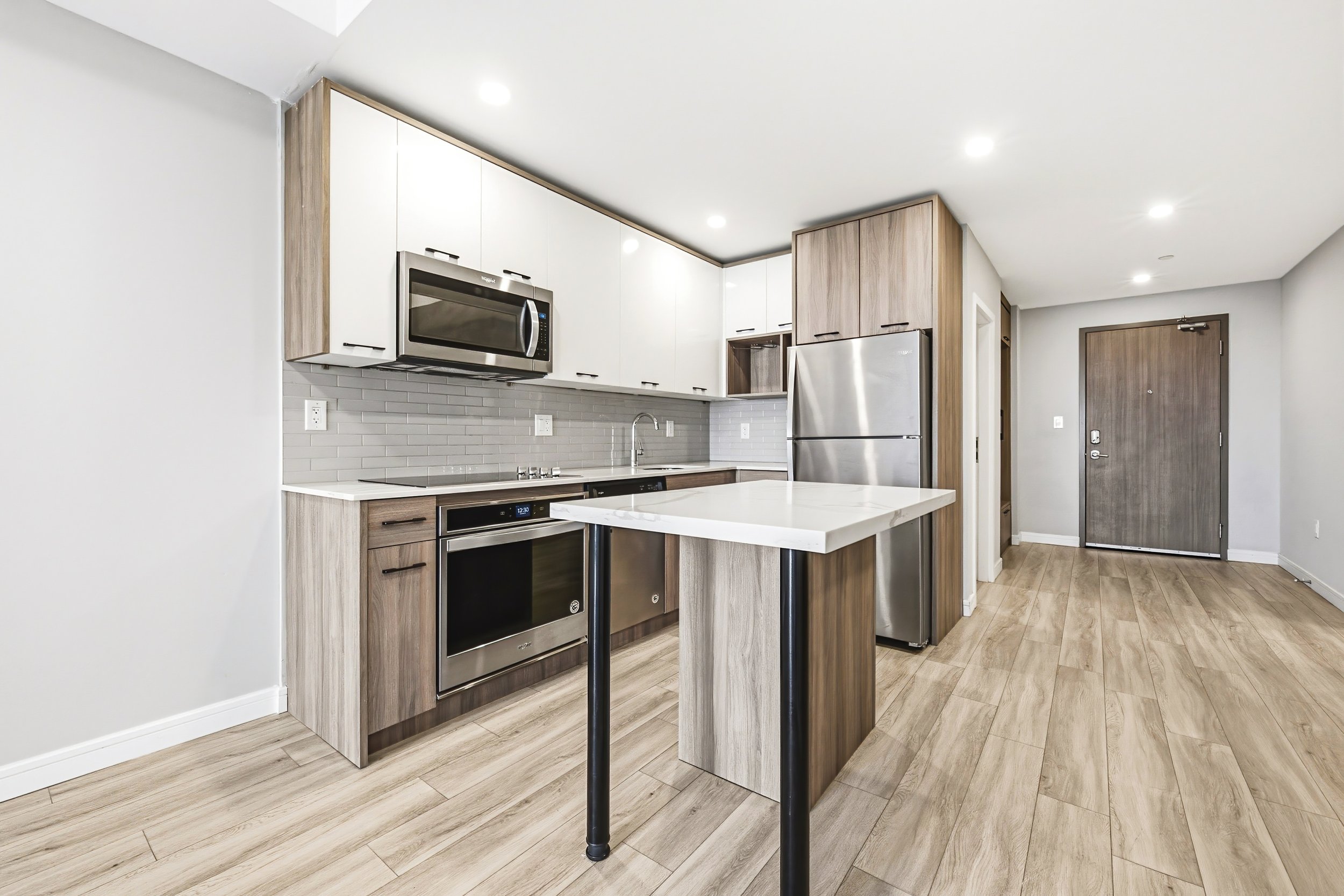 Modern kitchen with white and wood cabinets, stainless steel appliances, gray subway tile backsplash, and a small white dining table with black legs.