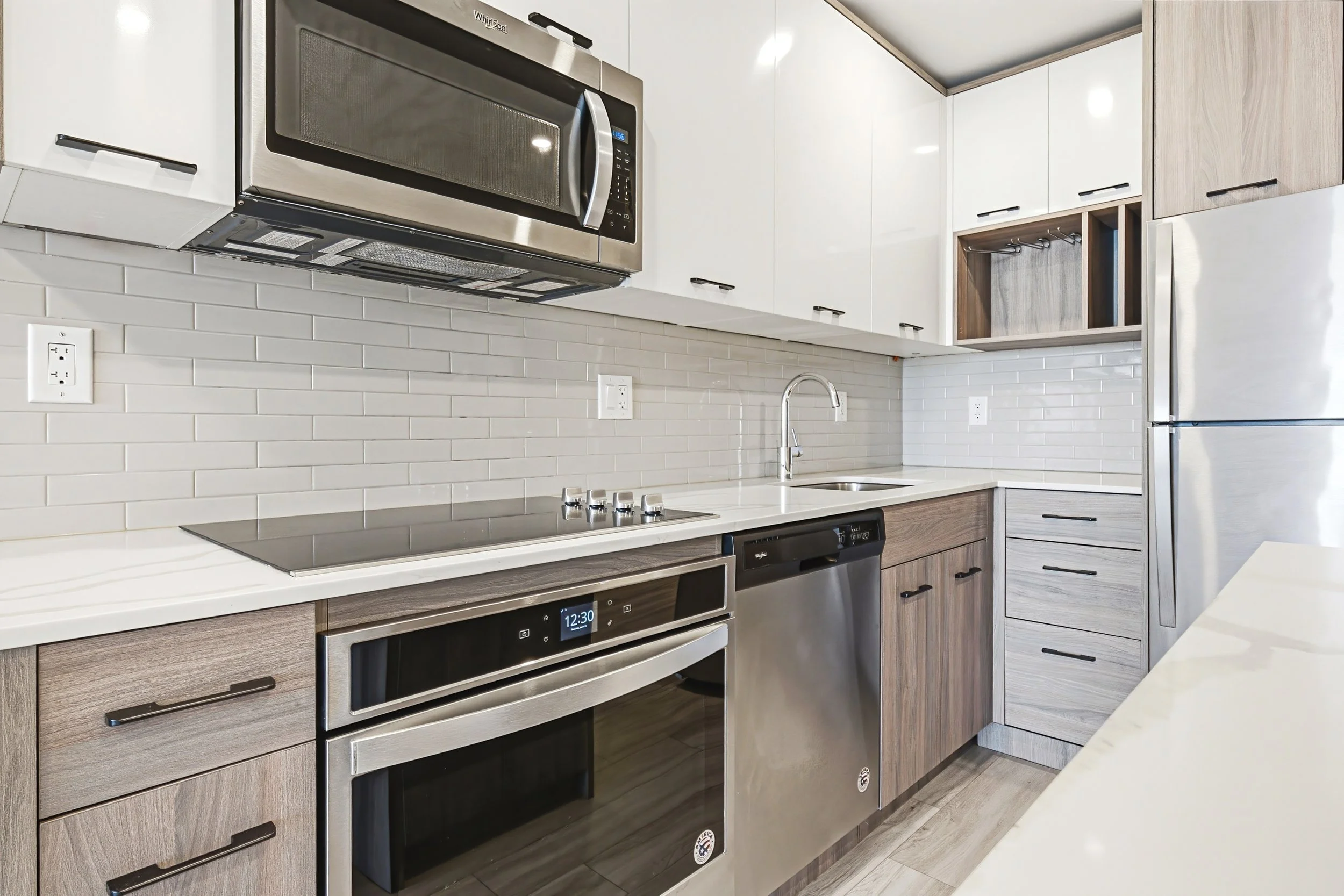 Modern kitchen with stainless steel microwave above the stove, white subway tile backsplash, wooden cabinets, and a stainless steel refrigerator.