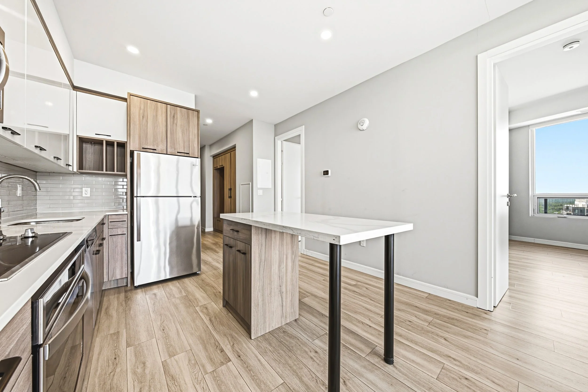 Modern kitchen with wood and white cabinetry, stainless steel appliances, a white marble island, and hardwood floors.