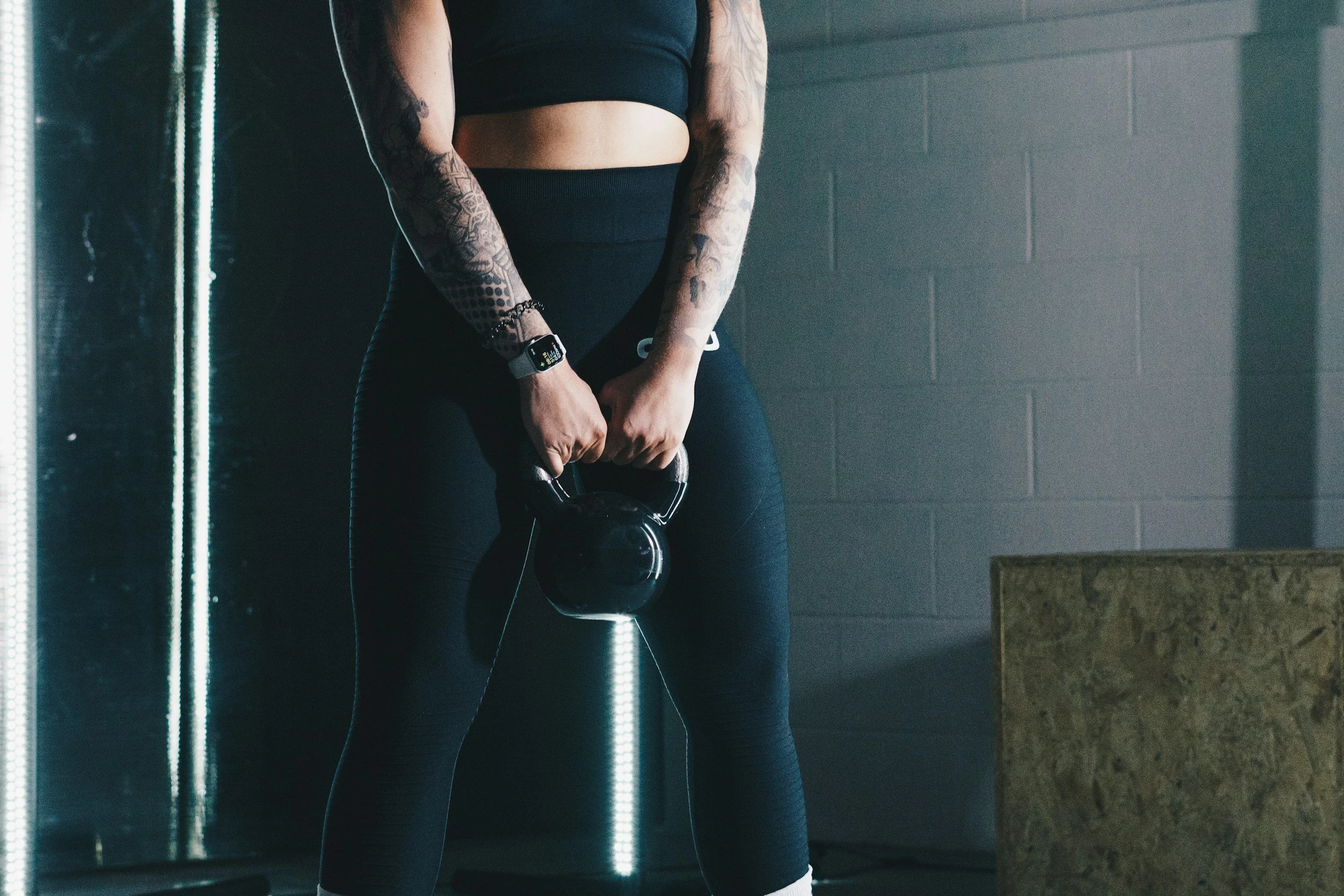 Person wearing black athletic clothing lifting a kettlebell in a gym.