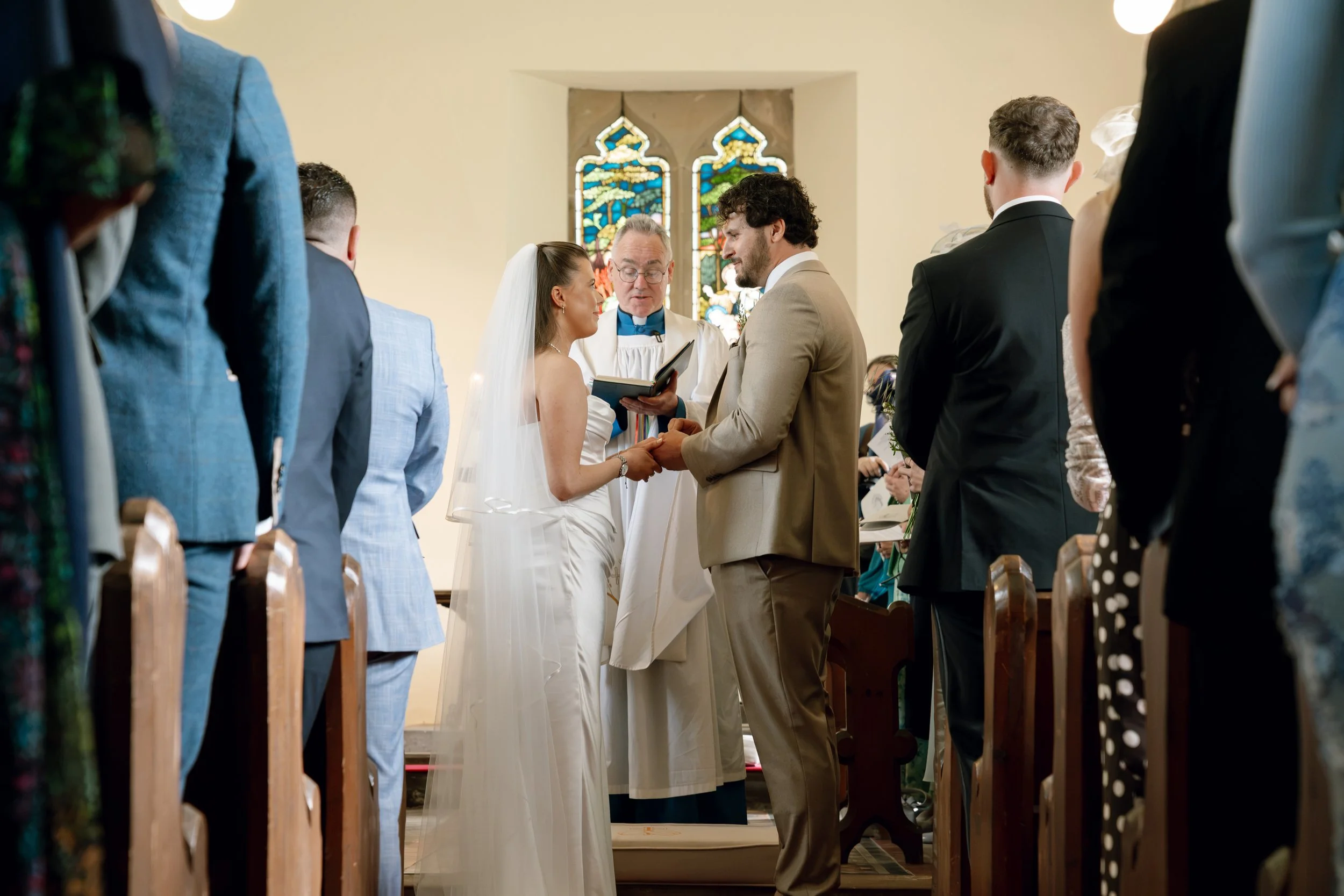 A couple exchanging wedding vows in a church with friends and family present, during a wedding ceremony.