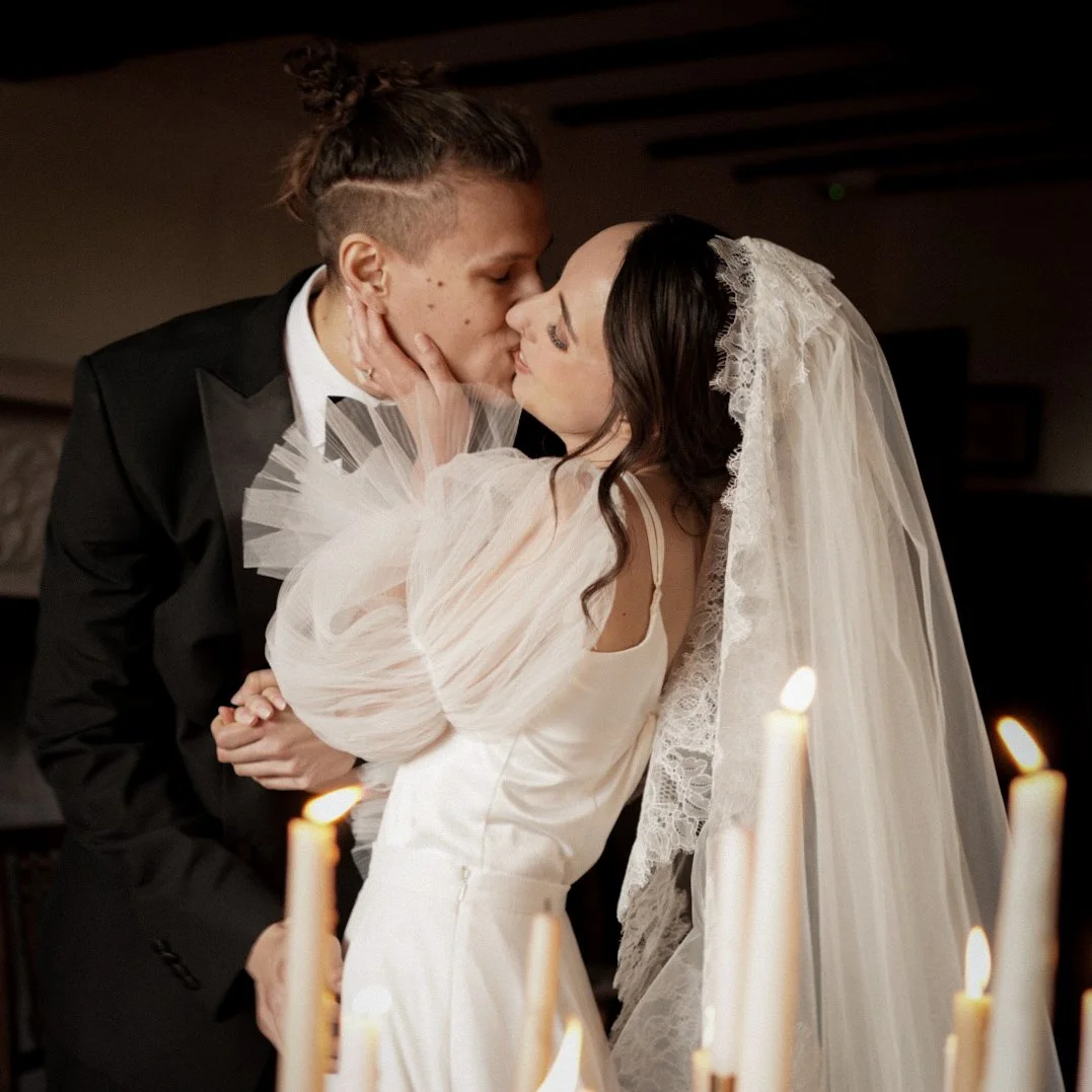 A bride and groom kissing in a wedding ceremony, with candles in the foreground.