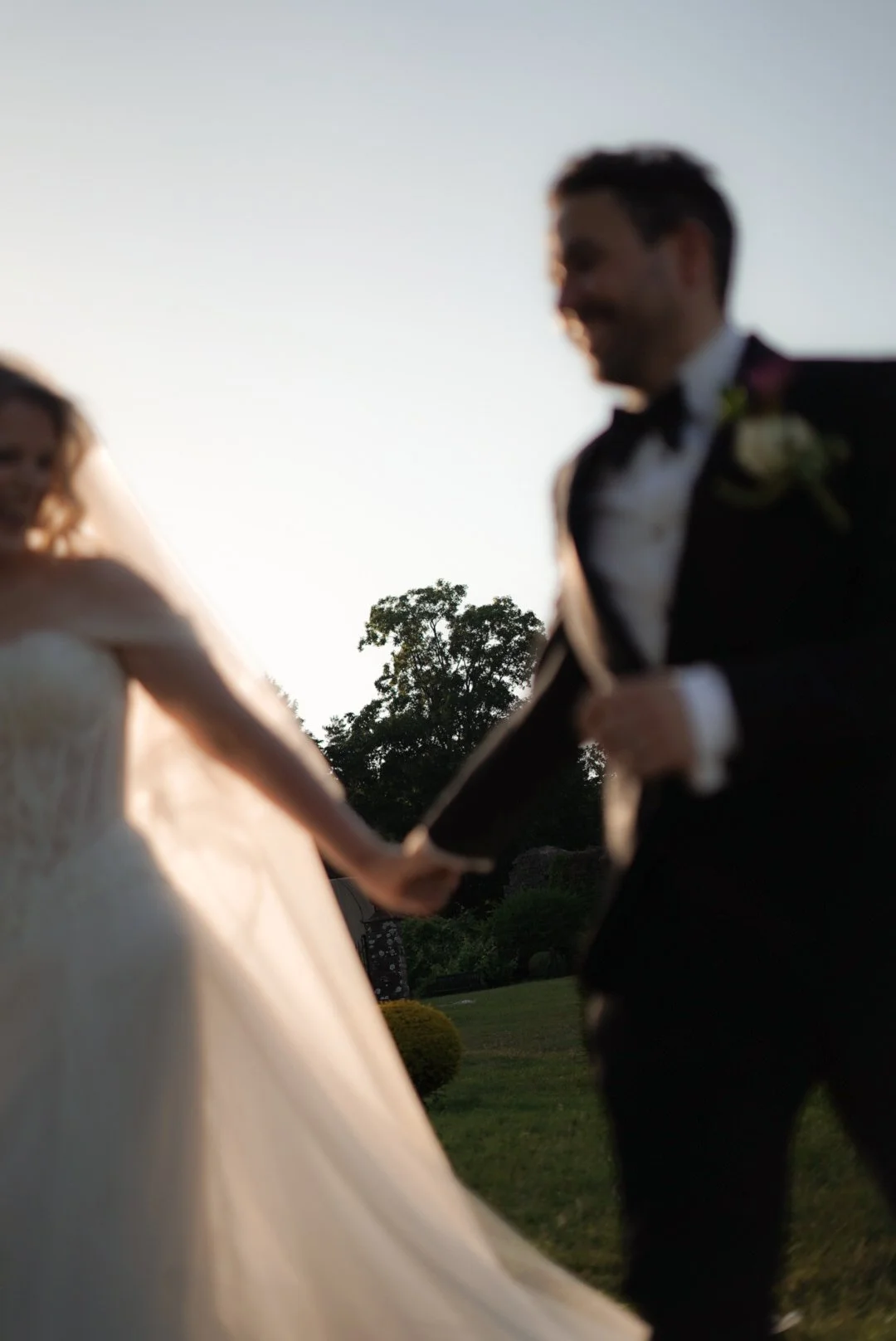 Blurry image of a bride and groom holding hands outdoors during sunset, with a tree in the background.