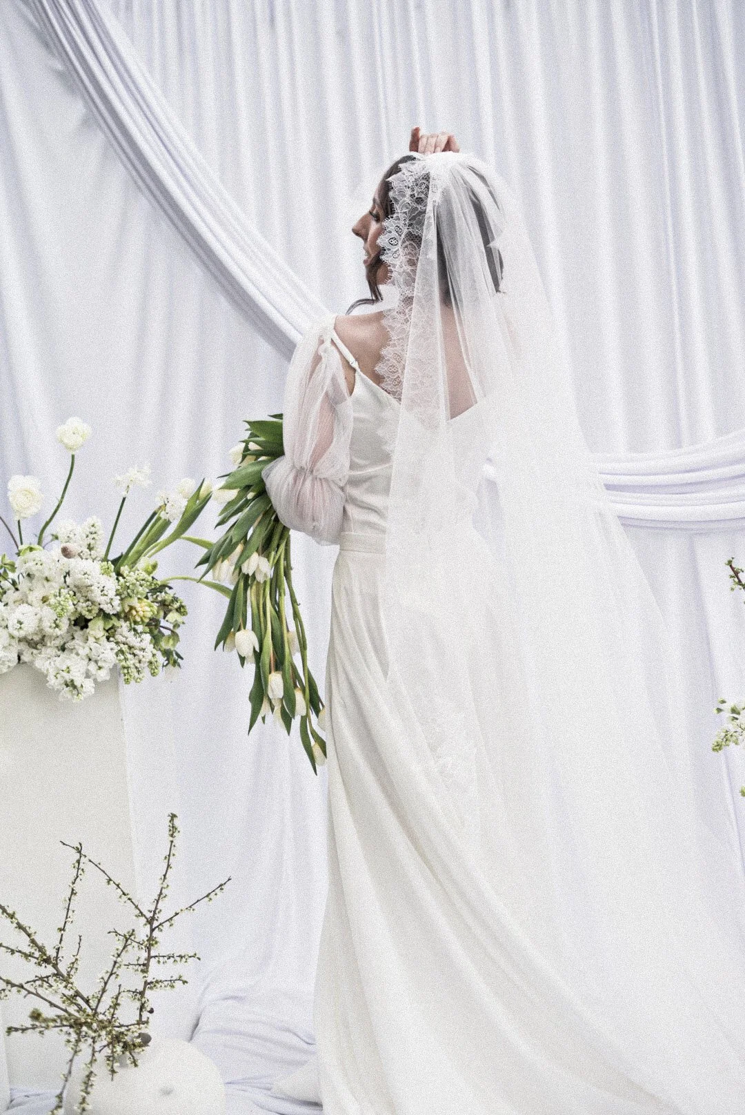 A bride in a white wedding dress and veil holding a bouquet of white flowers during a wedding ceremony.