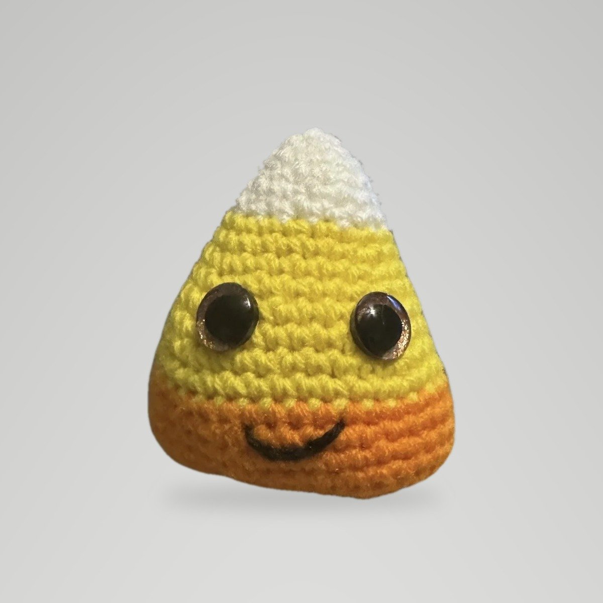 Handmade crochet candy corn plush in white, yellow, and orange with bronze safety eyes and a stitched smile