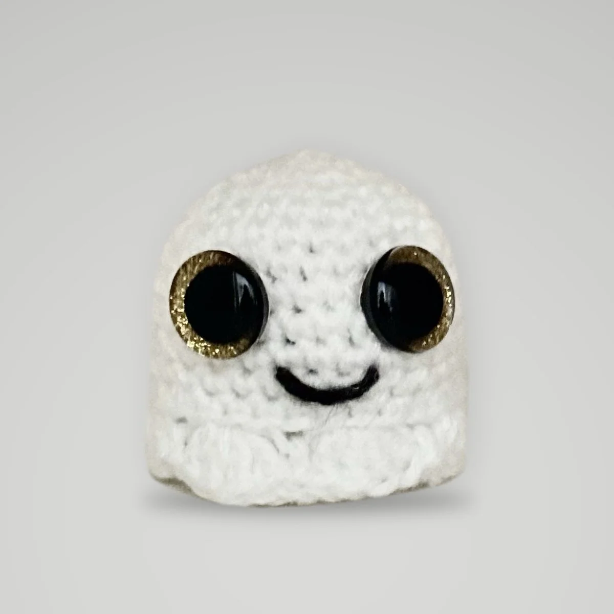 Handmade crochet ghost plush in white with gold-glitter safety eyes and a black stitched smile